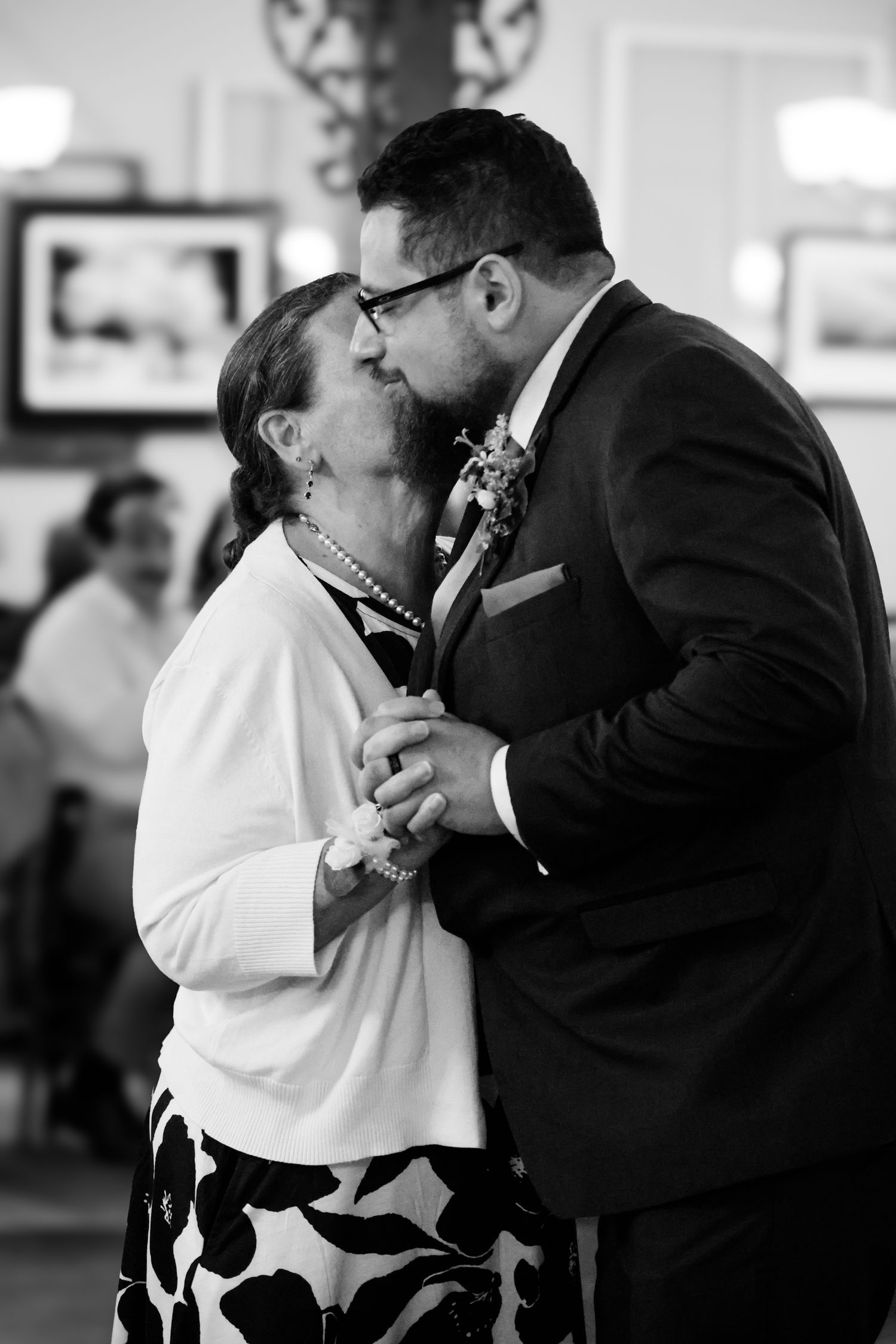 A tender black and white moment captured during a dance as a couple in formal attire share an intimate embrace.