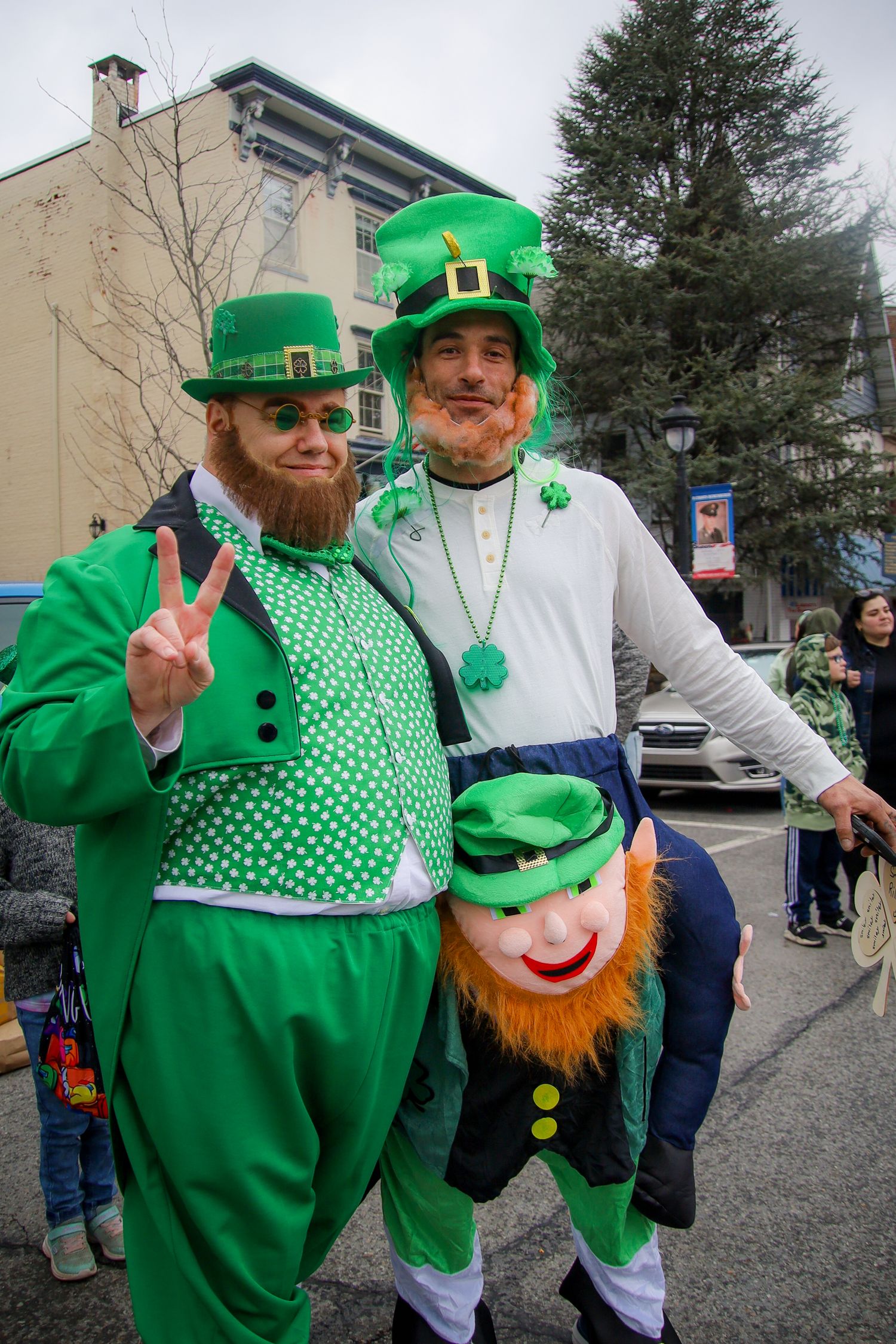 Festive St. Patrick's Day revelers wearing bright green leprechaun costumes and fake orange beards pose at outdoor celebration.
