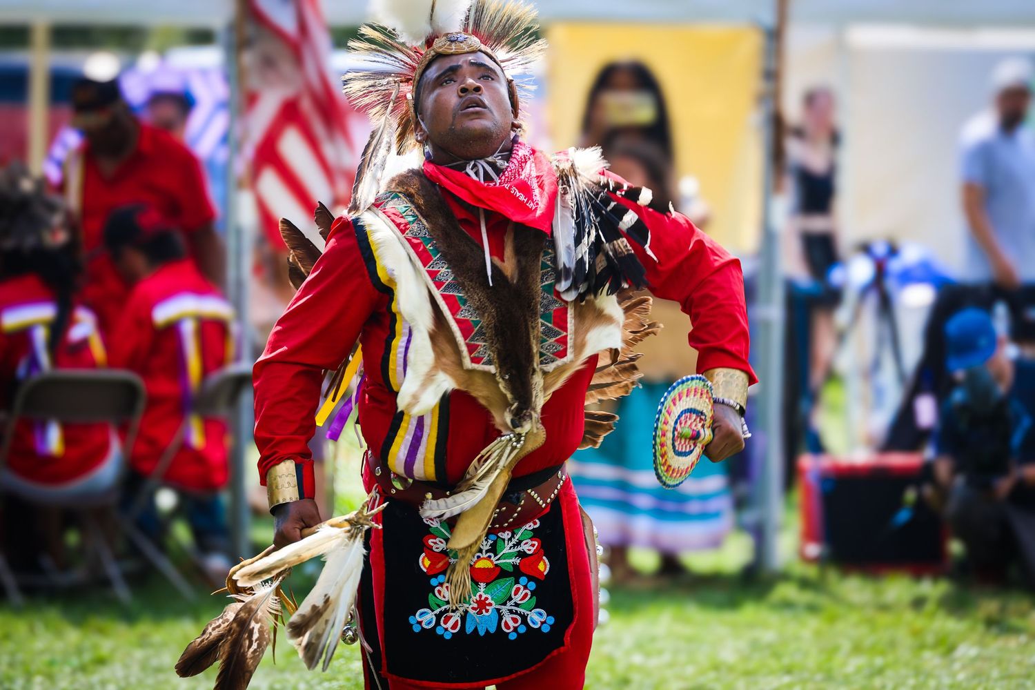 Native American dancers in traditional regalia perform at a powwow celebration with vibrant red and yellow outfits.