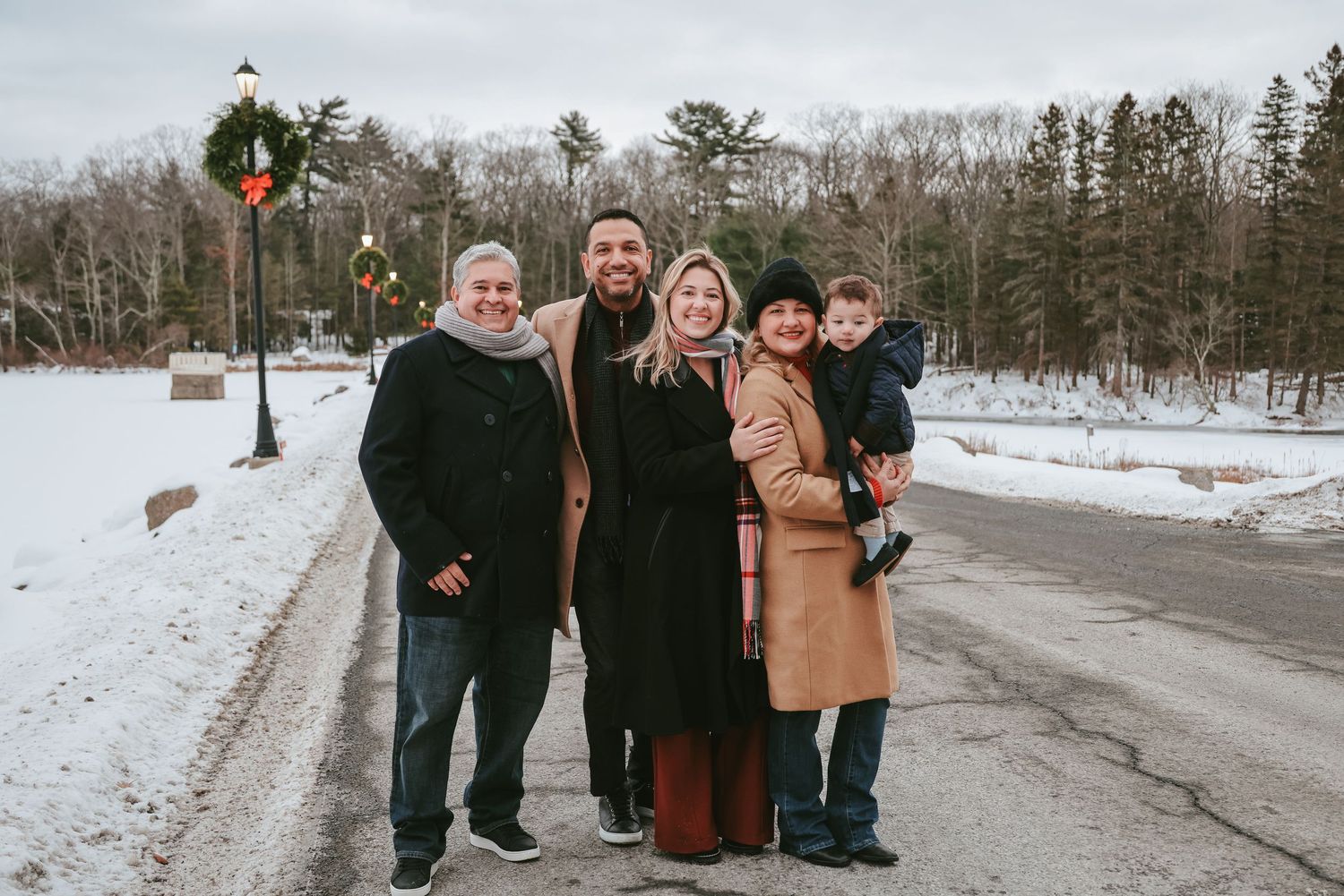 Family gathering outdoors on a snowy winter path surrounded by bare trees and evergreens.