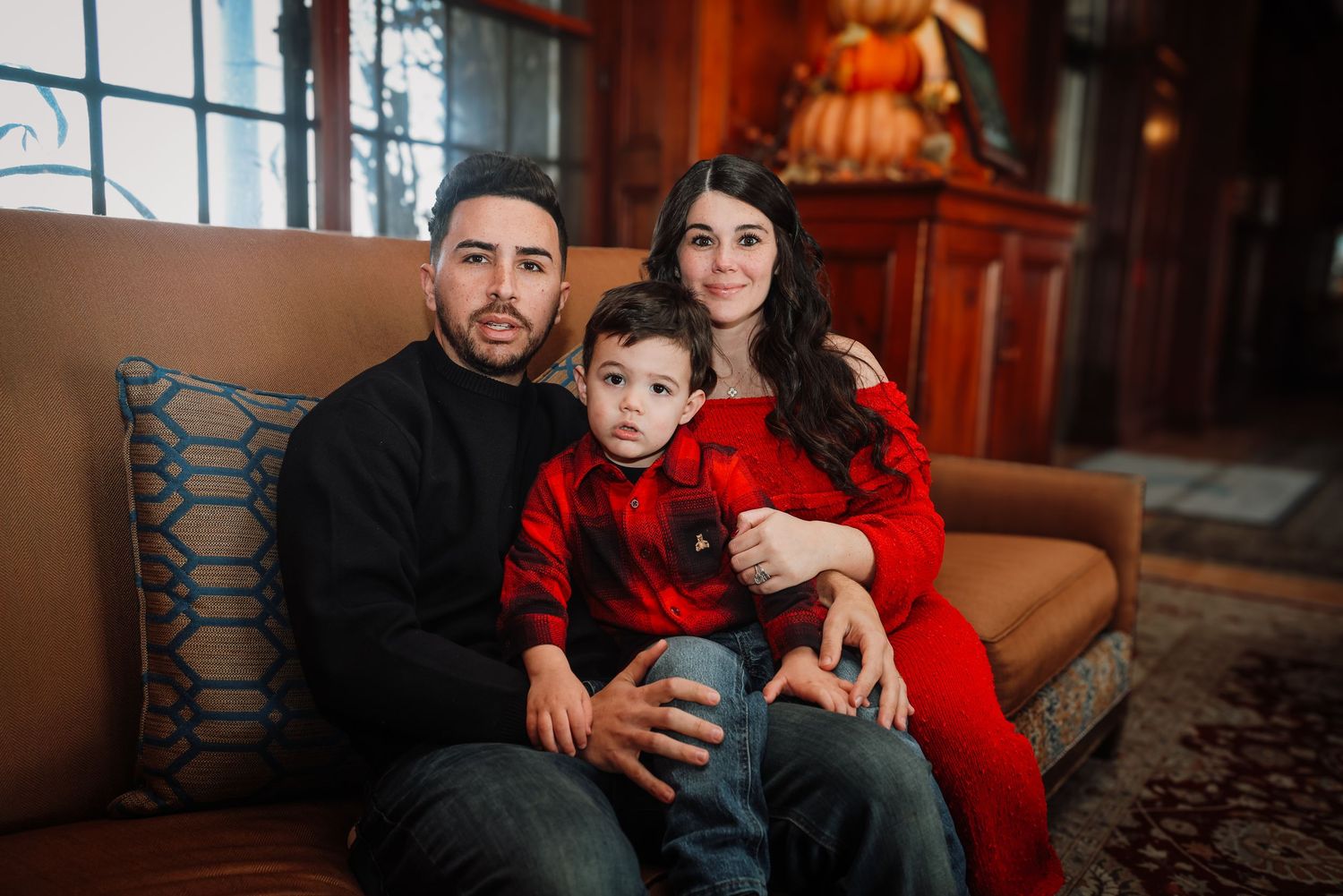 A family wearing coordinated red and black outfits poses together on a couch for holiday portraits.