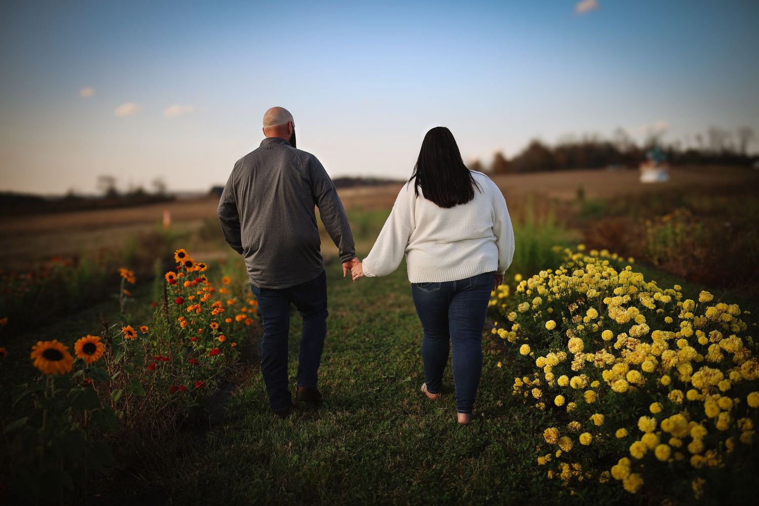 Two people walk together through a garden path with blooming yellow and orange flowers at sunset.