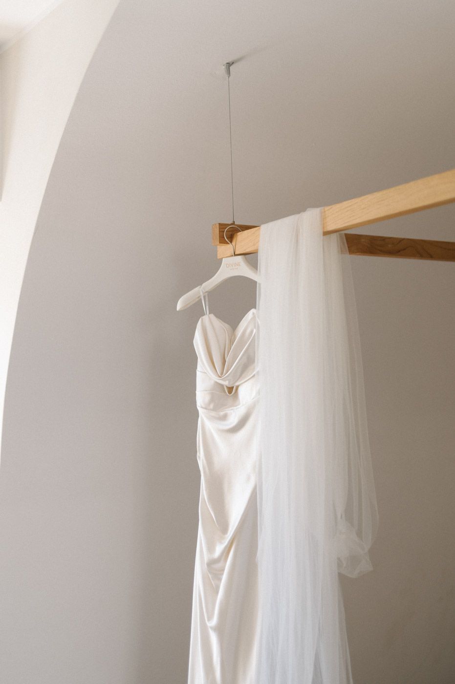 White wedding dress hanging elegantly against a minimalist white wall.