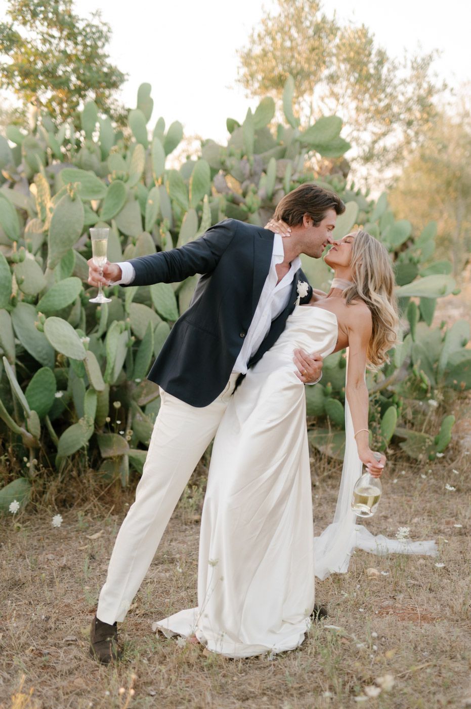 A romantic wedding couple dips and dances outdoors near desert cactus plants at sunset.