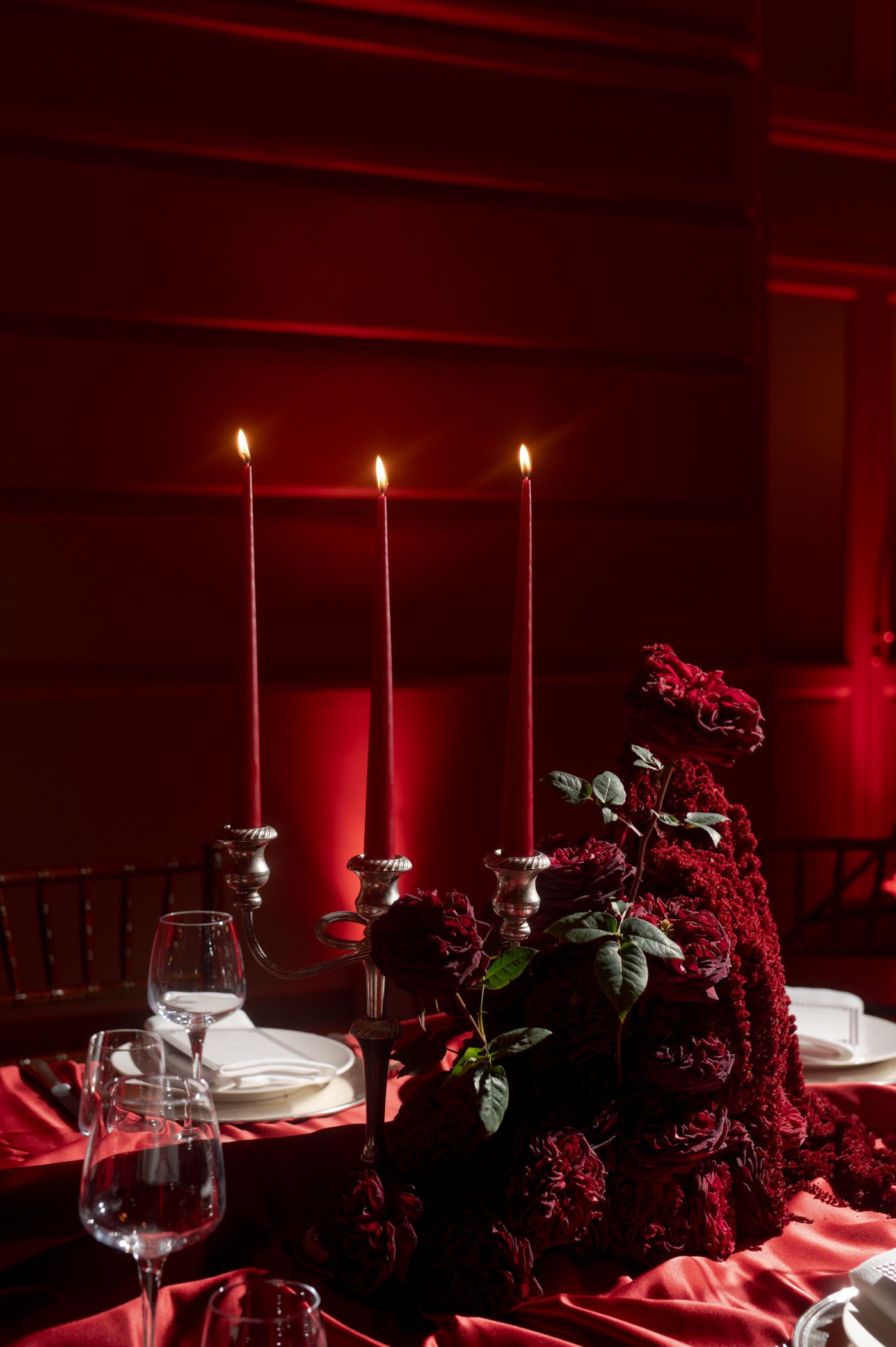 A romantic table setting with lit candles and dark red lighting creates an intimate dining atmosphere.
