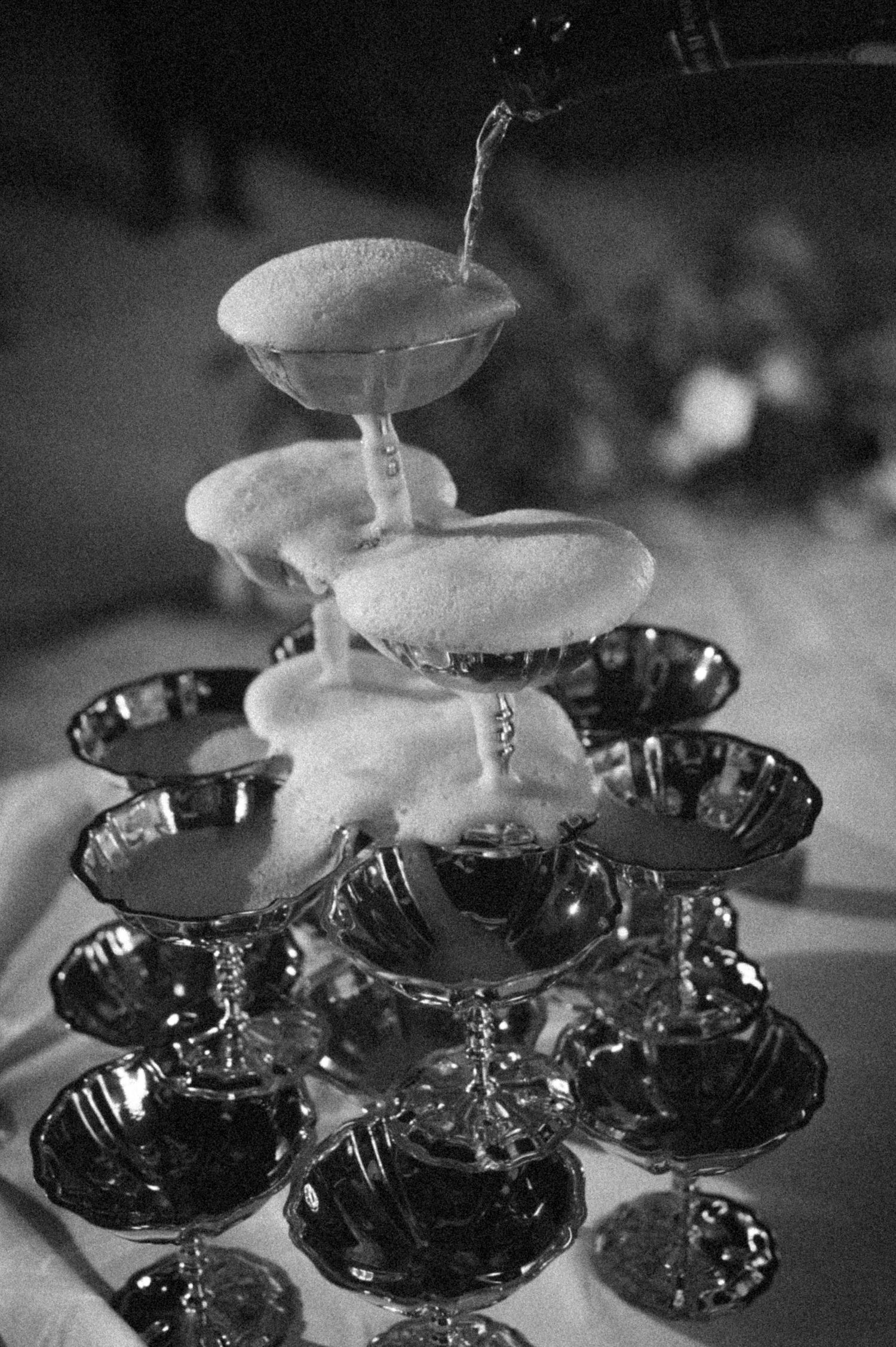 Black and white photo of a champagne tower overflowing with bubbly being poured from the top.