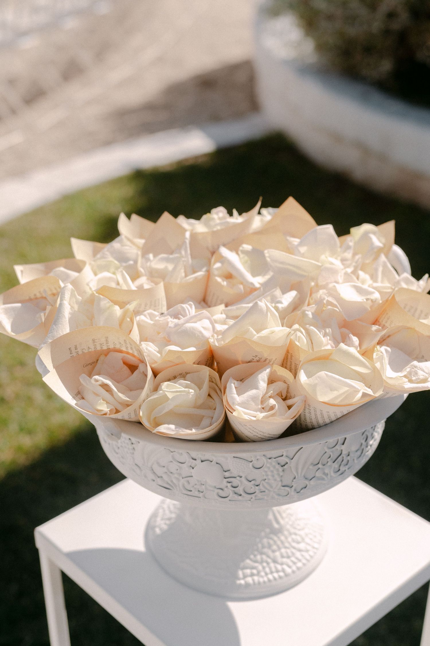 Elegant white pedestal bowl filled with cream paper cone favors for a wedding ceremony outdoors.