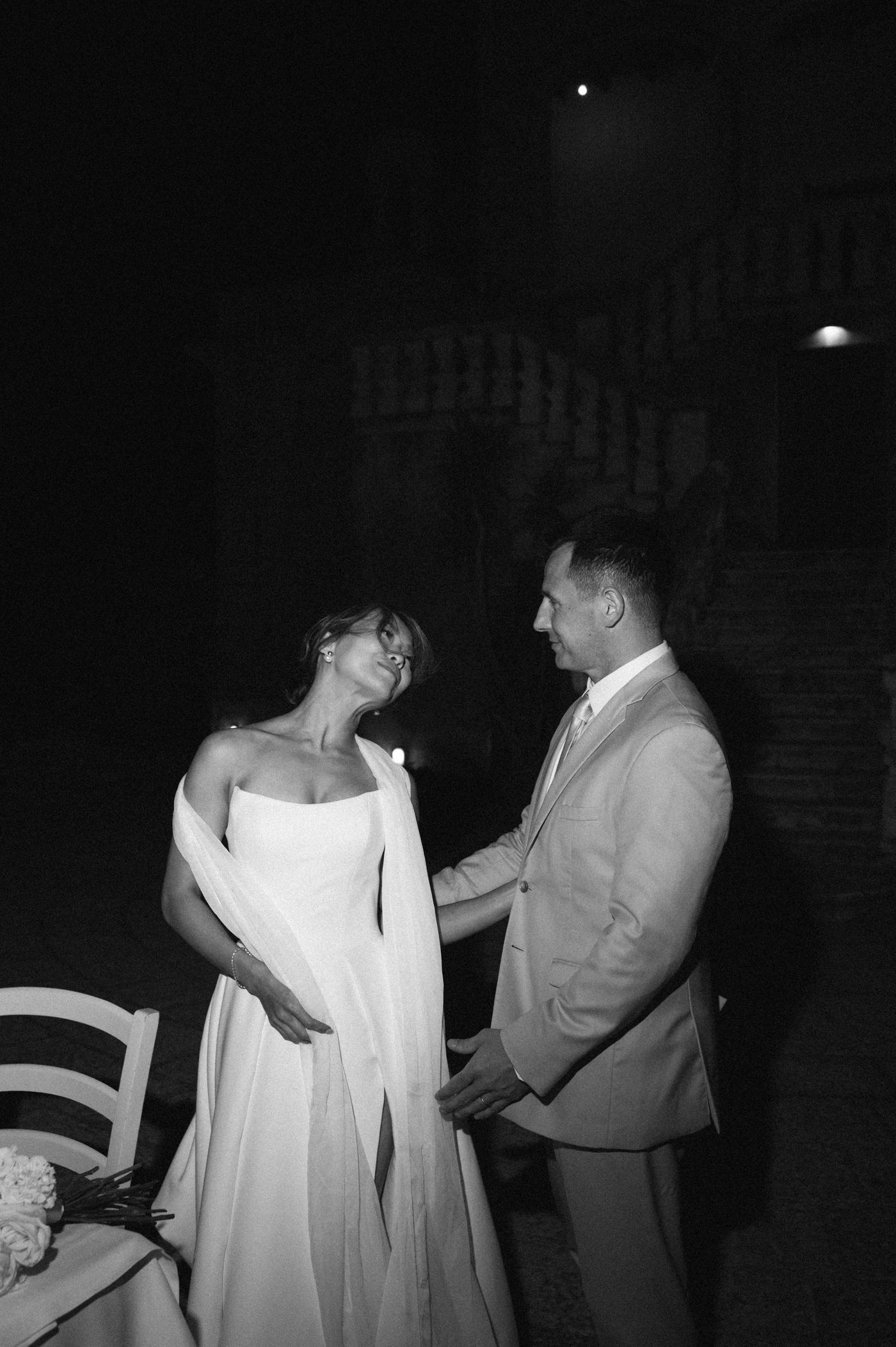 A couple in formal attire dances together in a dimly lit setting, with the woman wearing a flowing white dress.