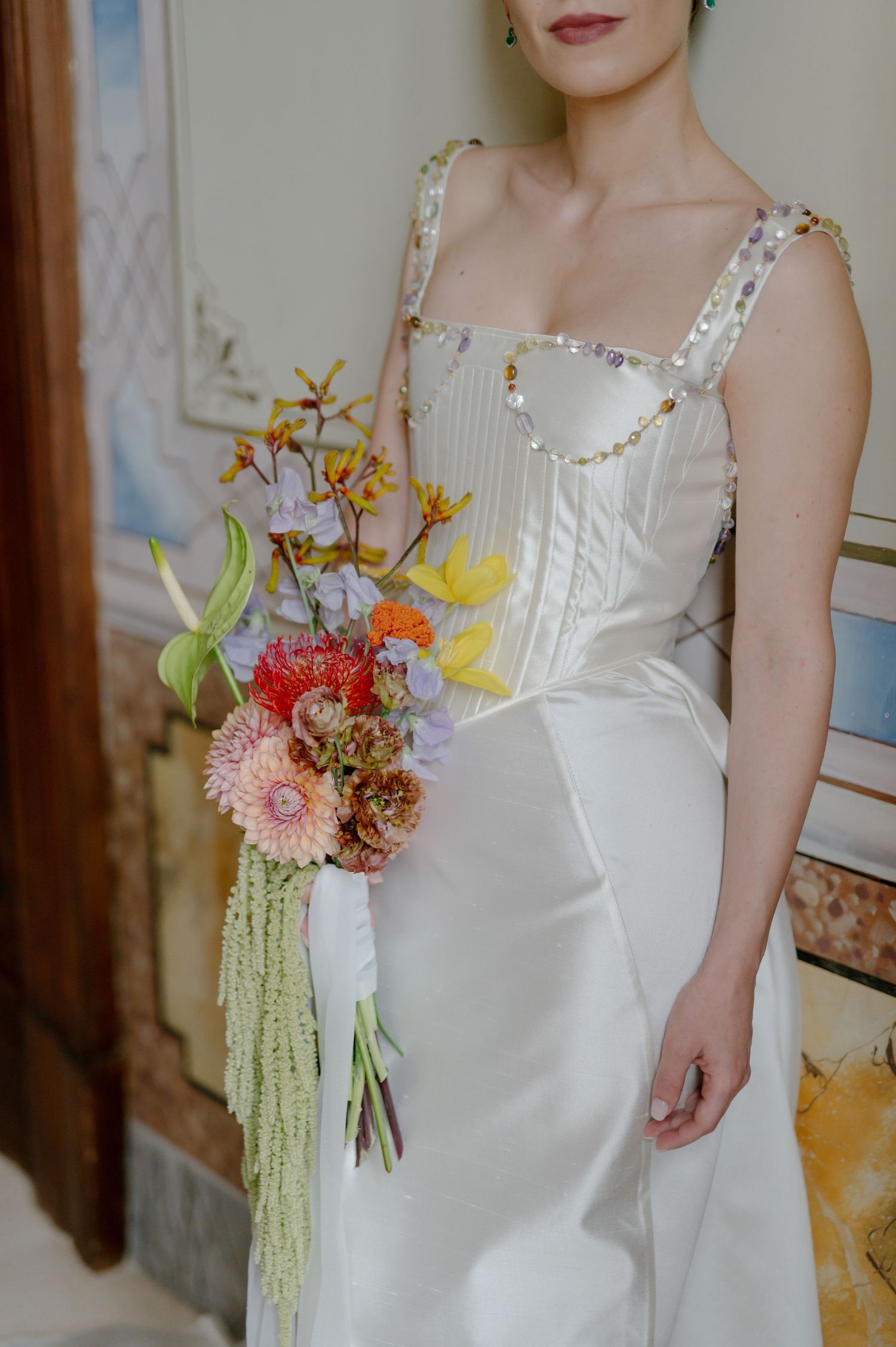 Close-up details of a white wedding dress with floral bouquet featuring pink and orange blooms and cascading greenery.