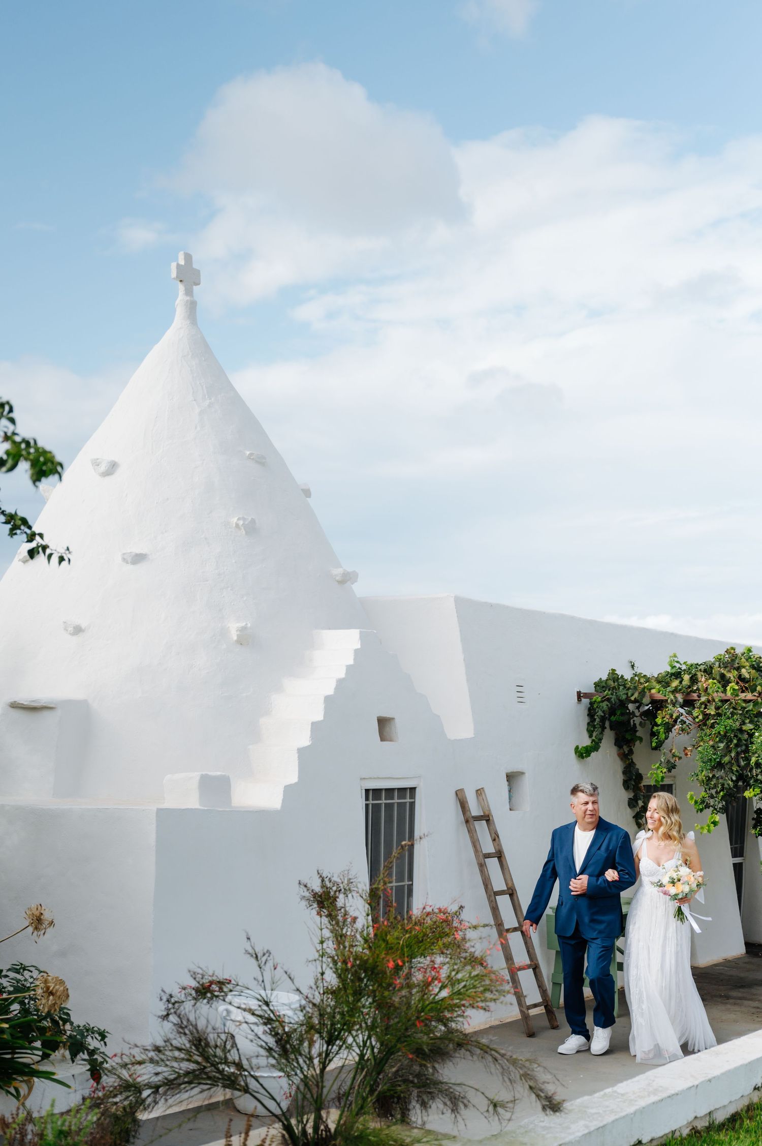 White Mediterranean buildings with unique architectural details and wooden ladder against bright blue sky.