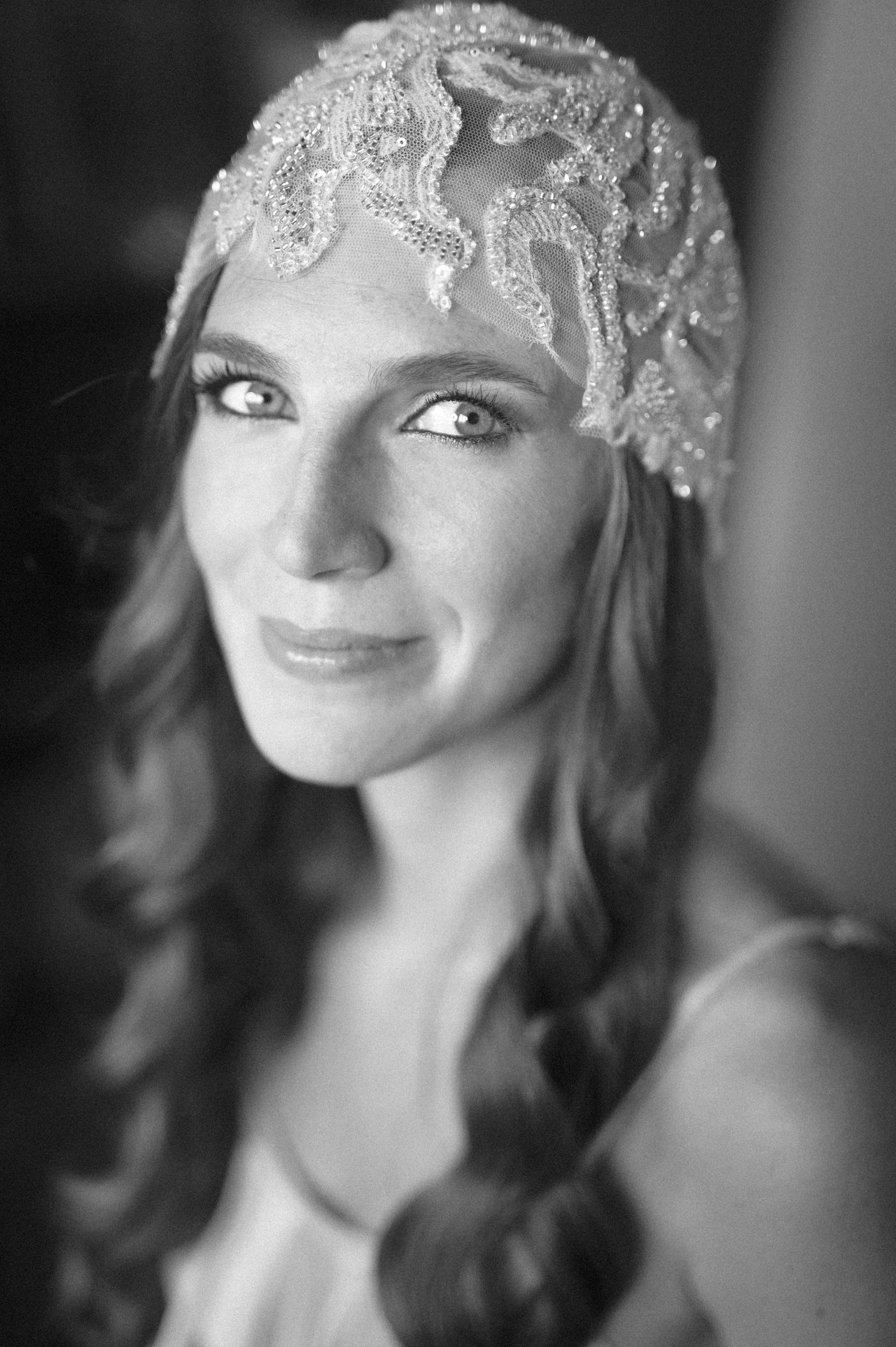 Black and white portrait of a bride wearing an ornate beaded lace headpiece with wavy hair and a gentle smile.