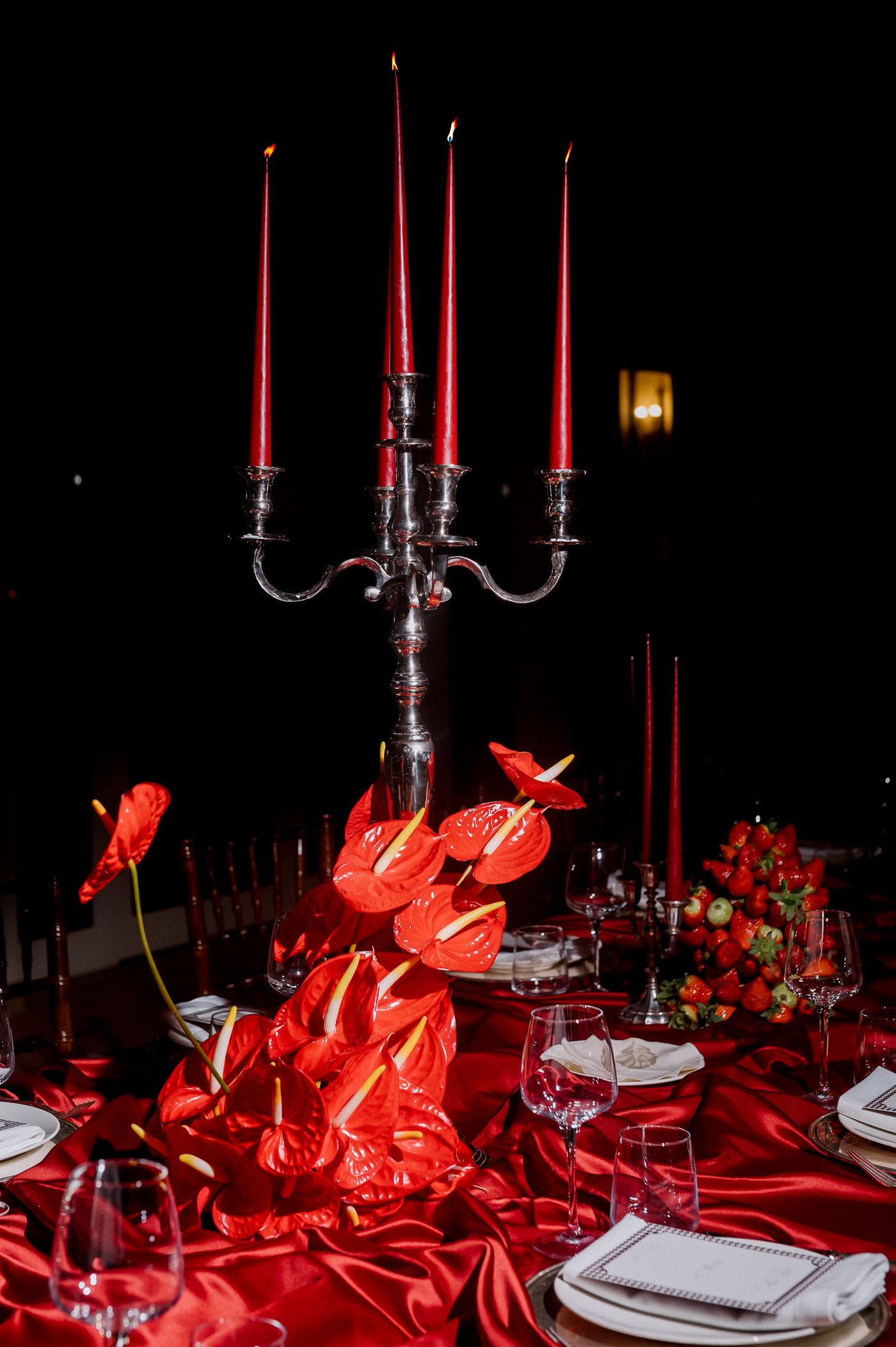 Elegant table setting with silver candelabra, red candles, and lobster decorations on dramatic red satin tablecloth.