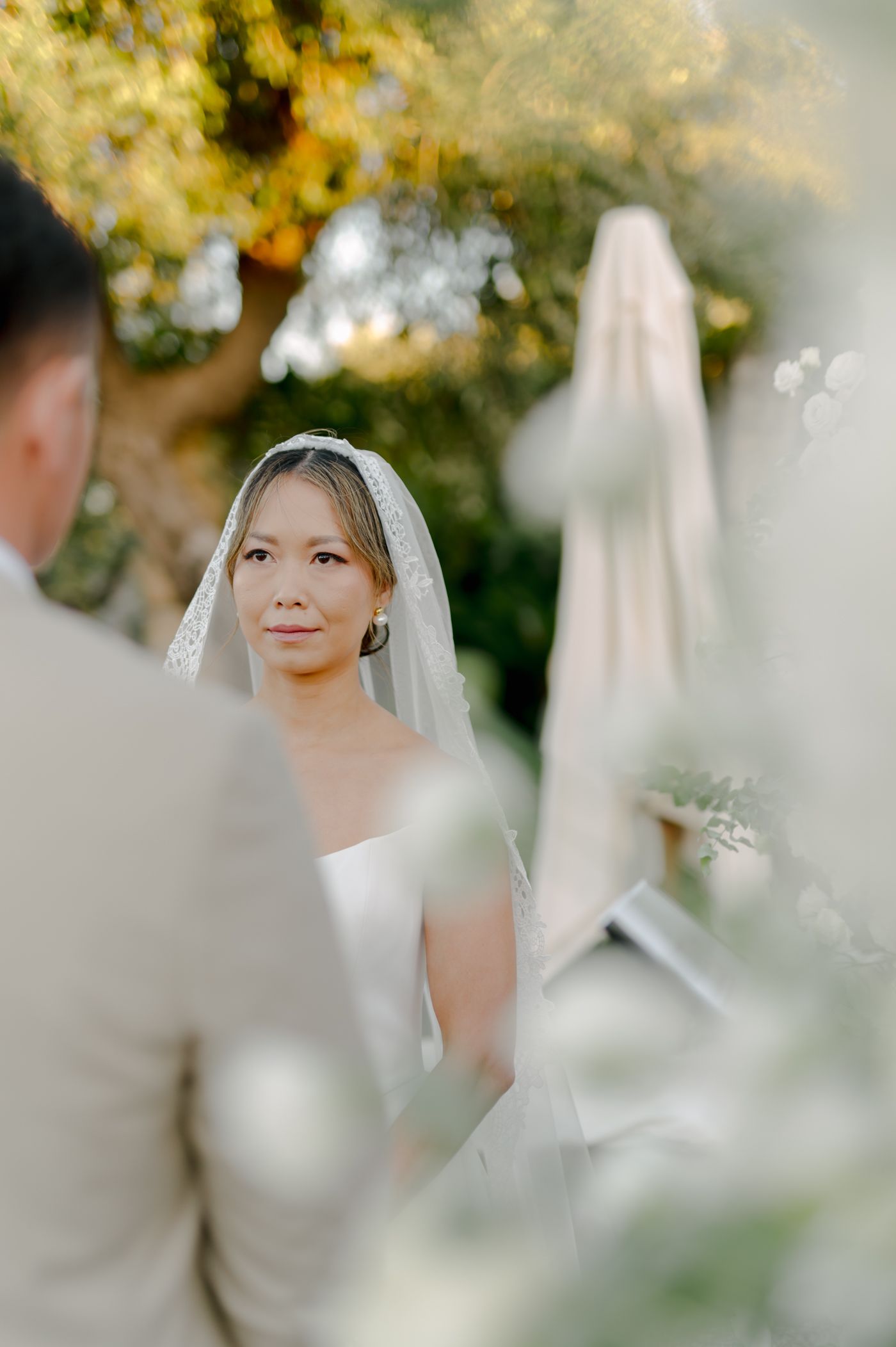 A dreamy wedding scene captured through soft focus with white floral arrangements and natural outdoor lighting.