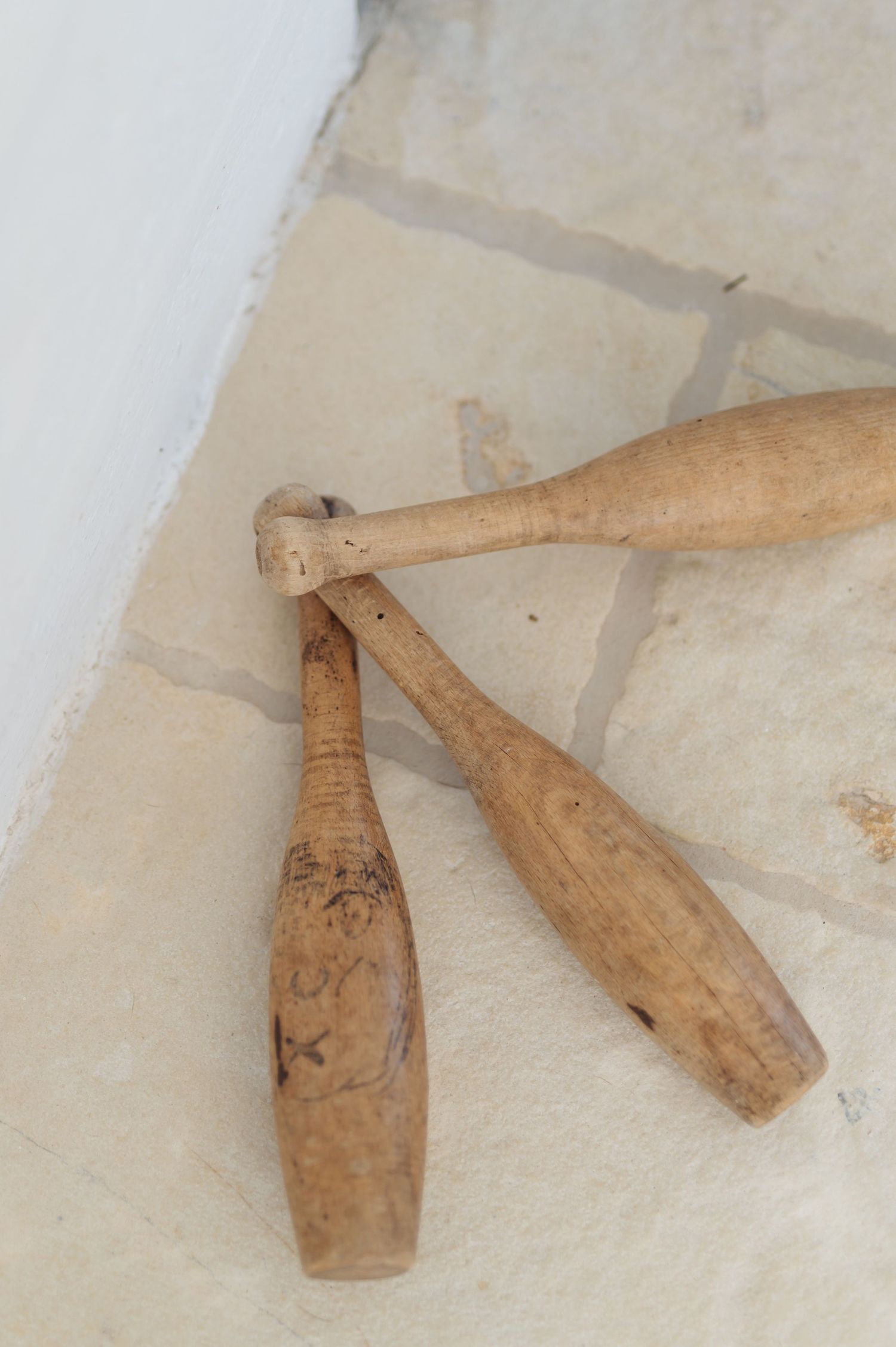 Three old wooden juggling pins or clubs with worn natural finish lying on a light colored surface.