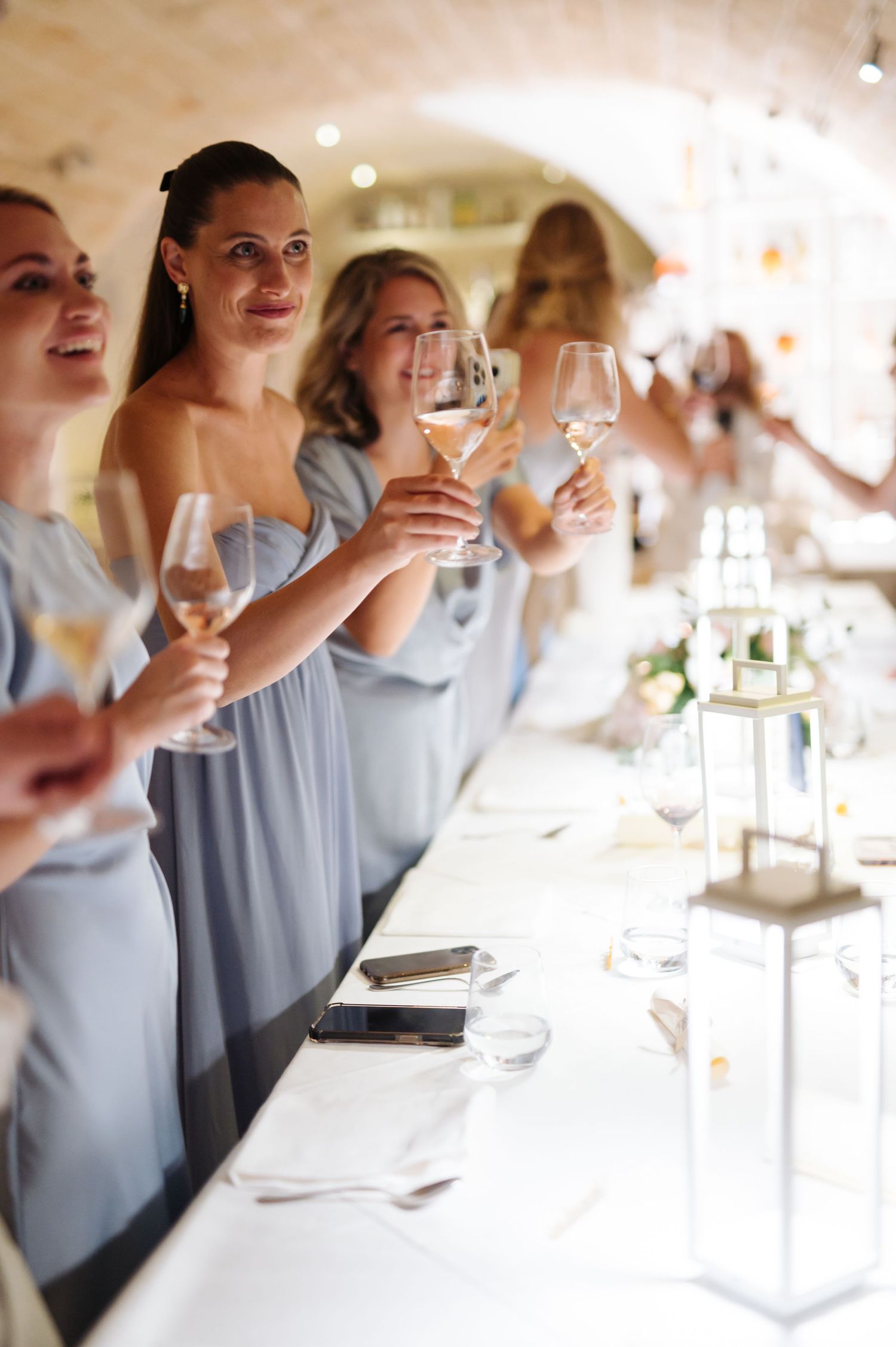 Bridesmaids in pale blue dresses raise wine glasses during a wedding celebration.