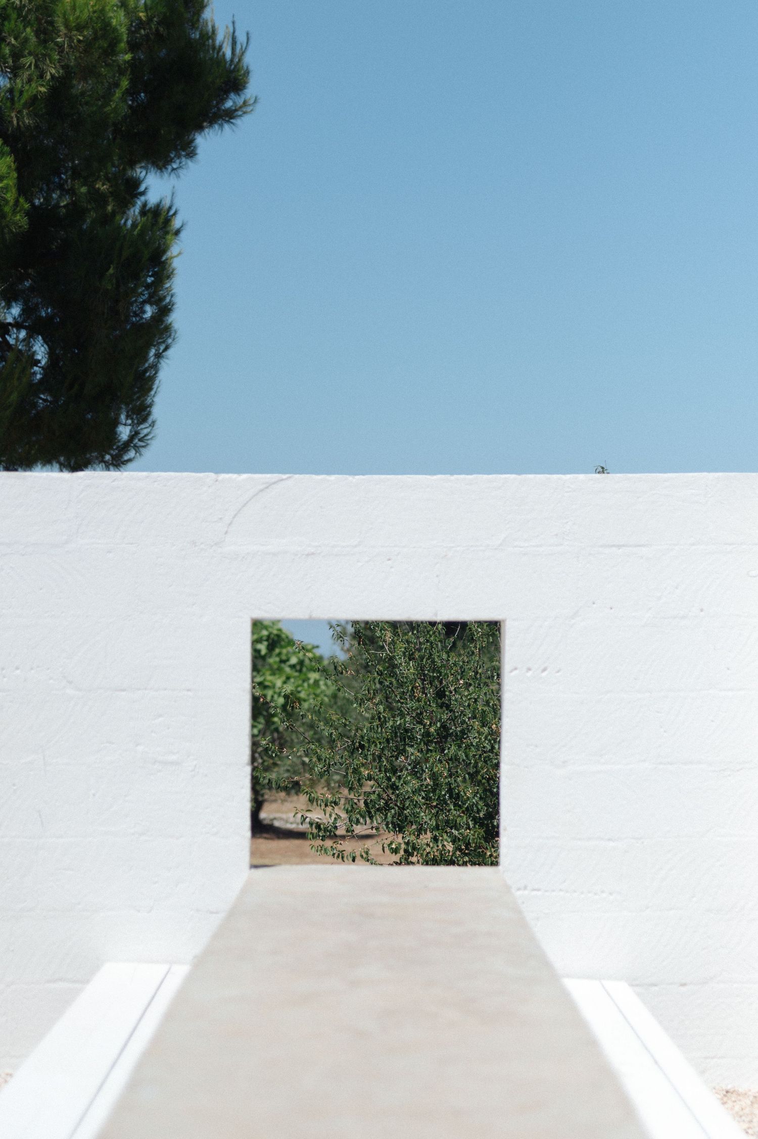 White architectural wall with small window openings against a bright blue sky.