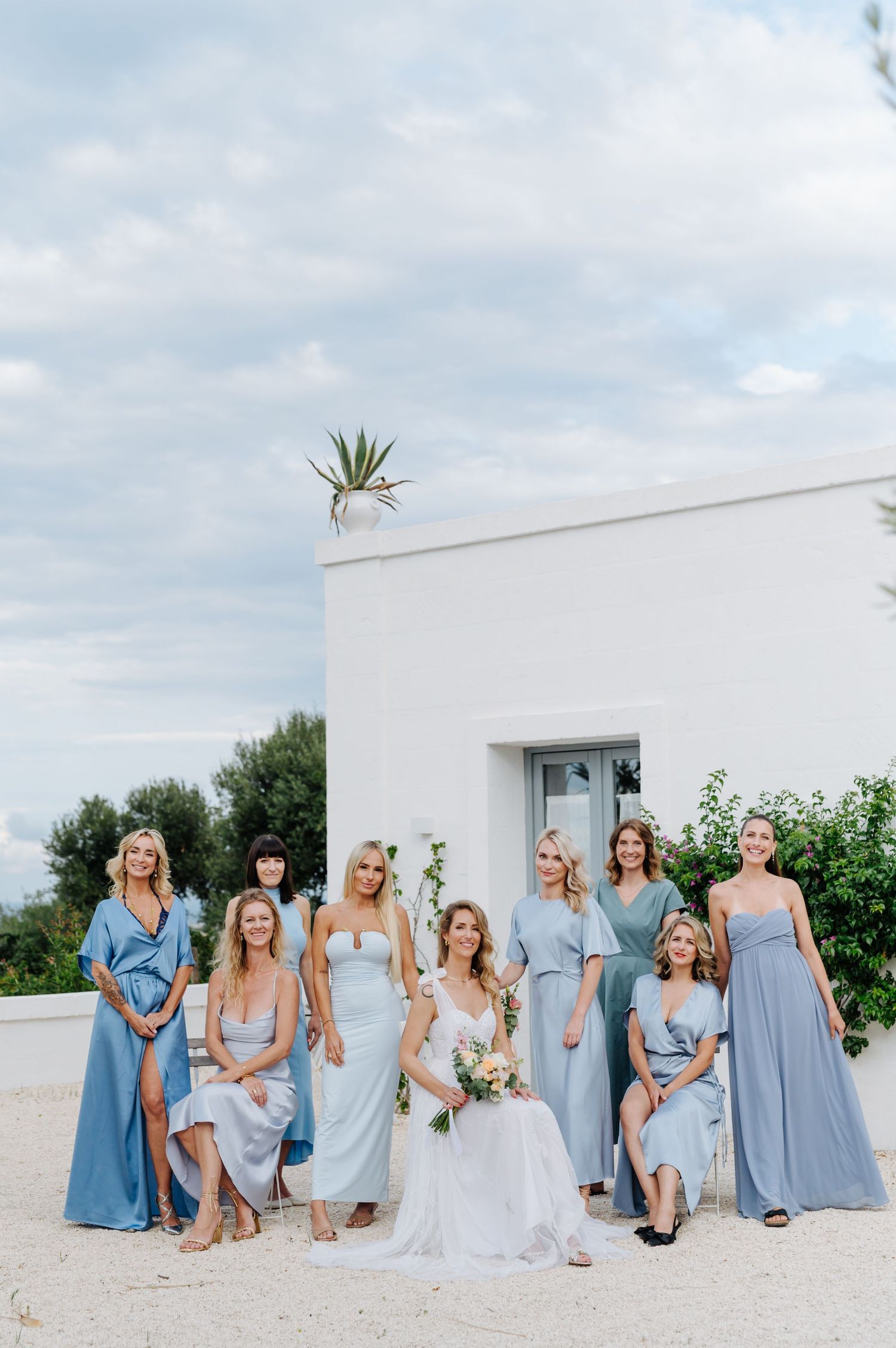 Wedding party in light blue dresses posing in front of a white Mediterranean building.