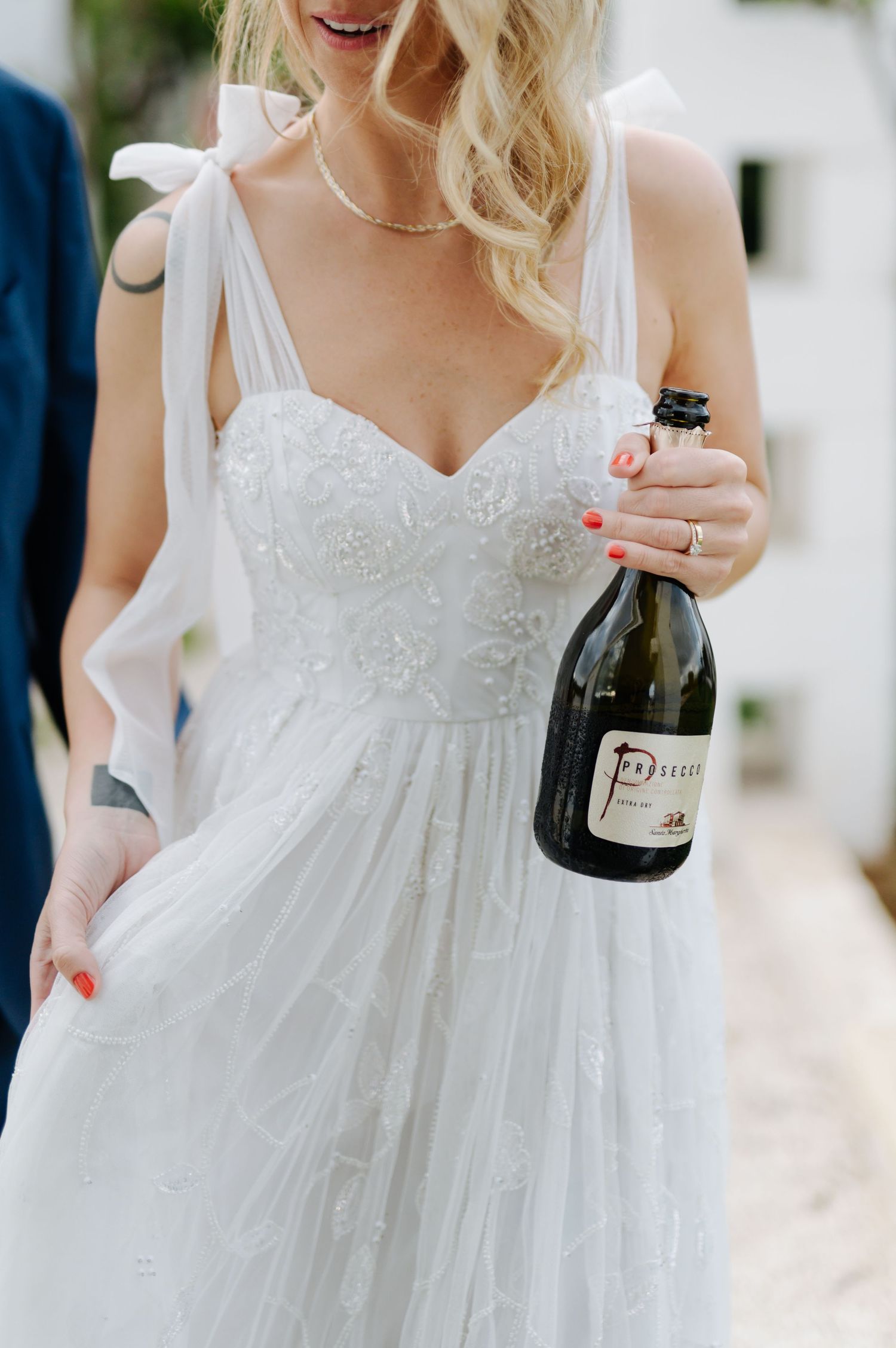 Detail of a white lace wedding dress with champagne bottle.