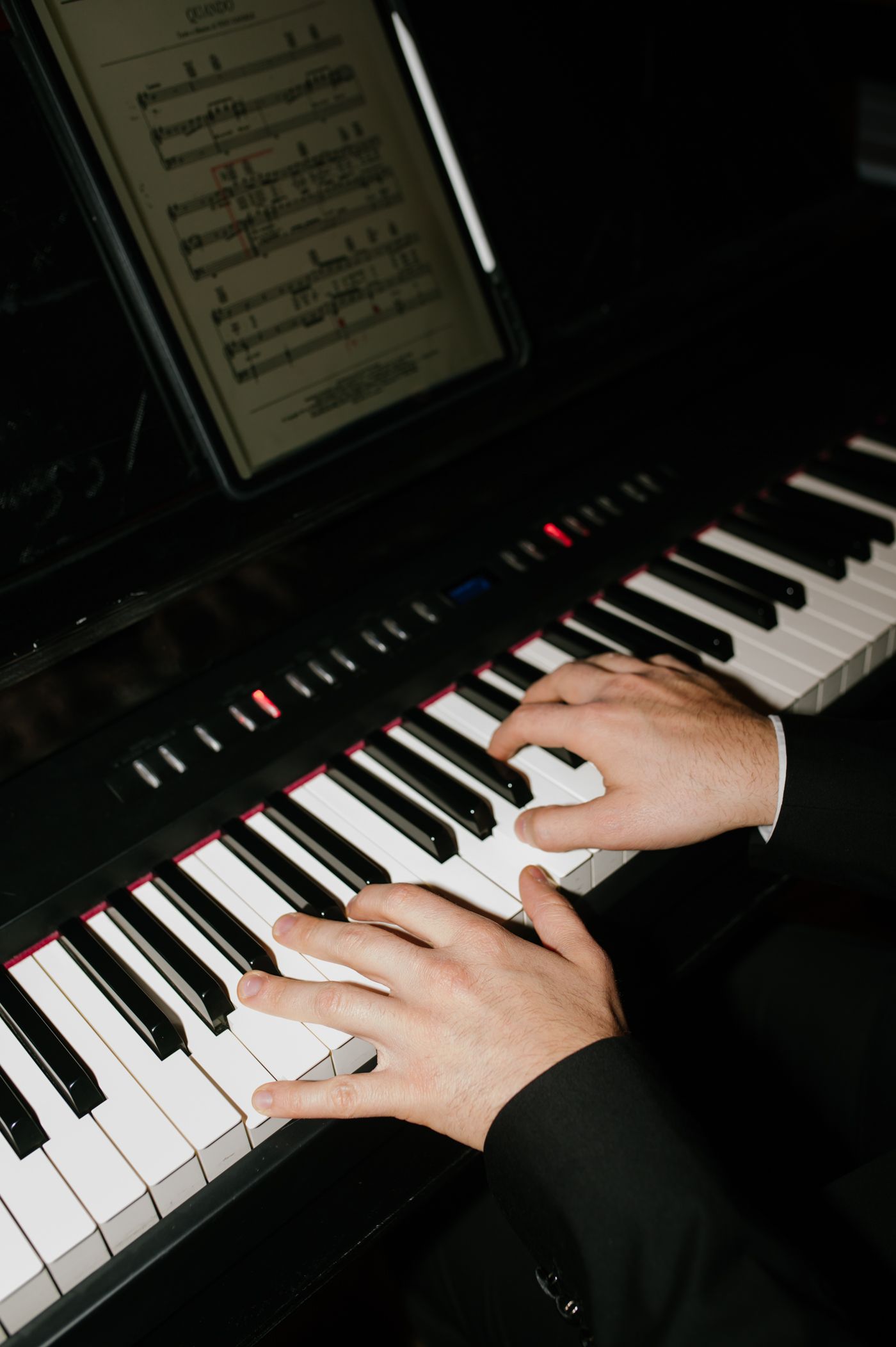 Hands playing a piano keyboard with sheet music visible in the background, showing progression of movement.