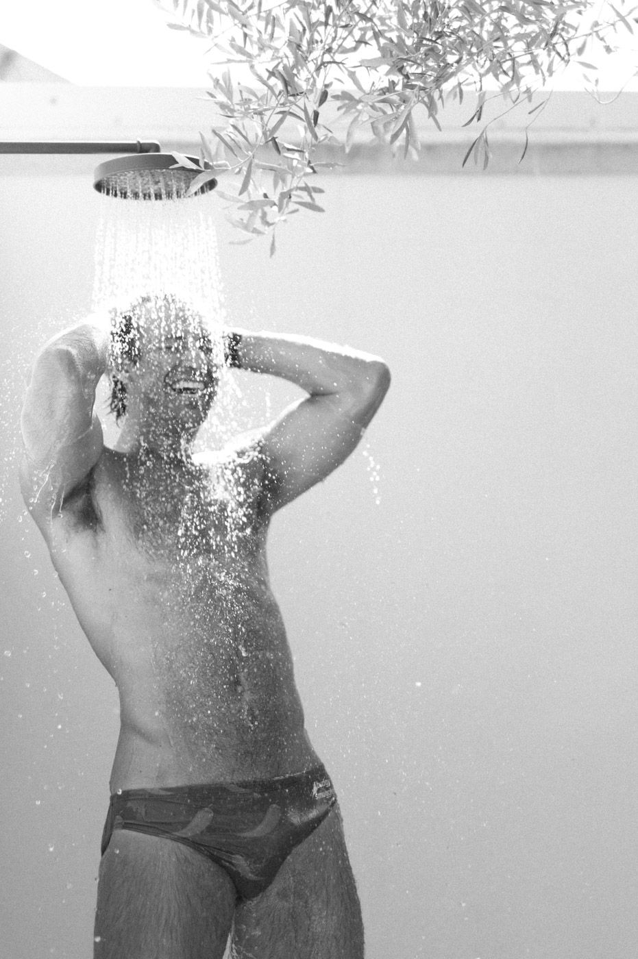 Person enjoying an outdoor shower beneath olive tree branches.