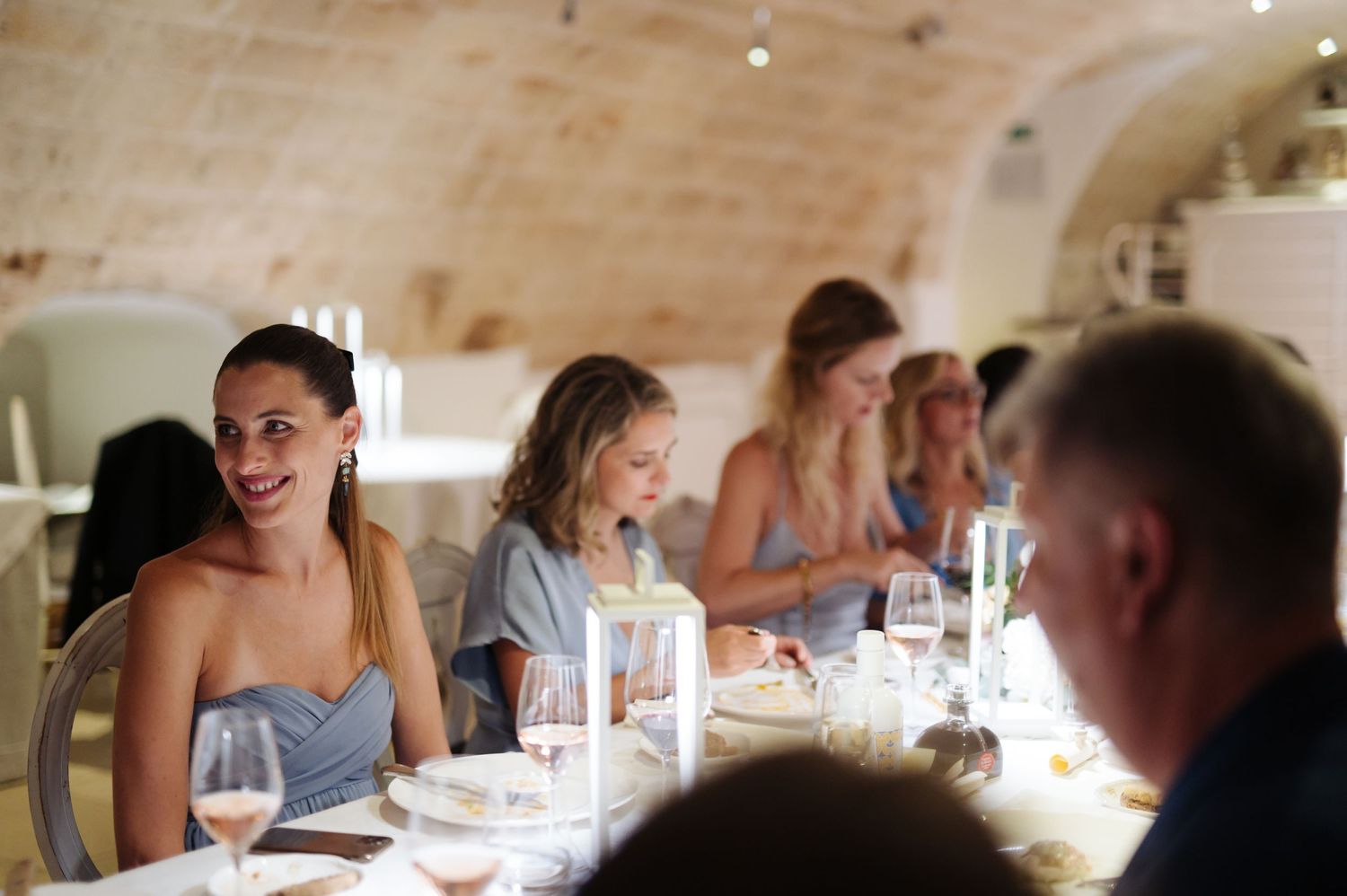 Wedding reception guests seated at long tables in a rustic stone dining room.