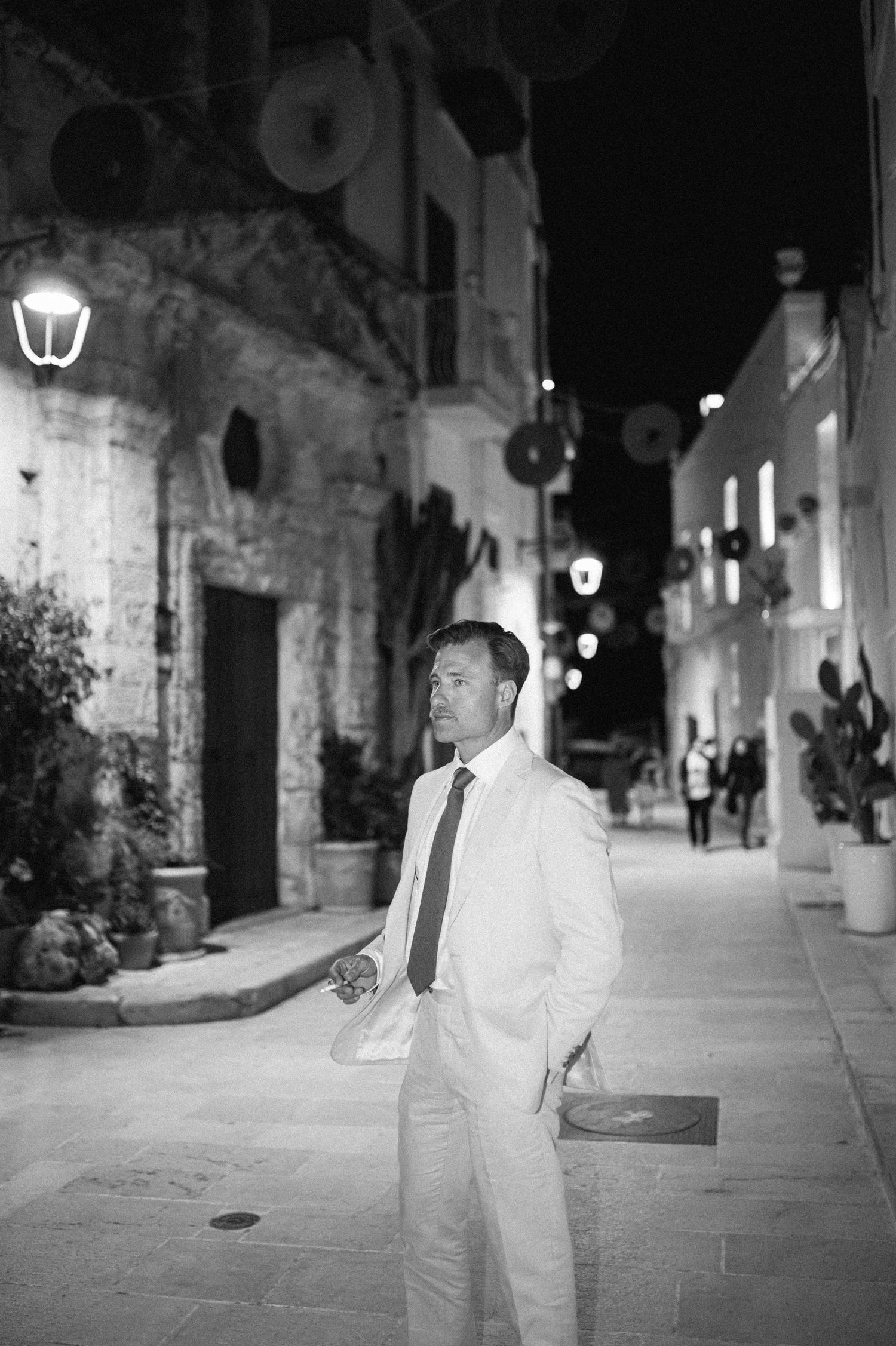 Person in light-colored suit walking along illuminated stone street at night.