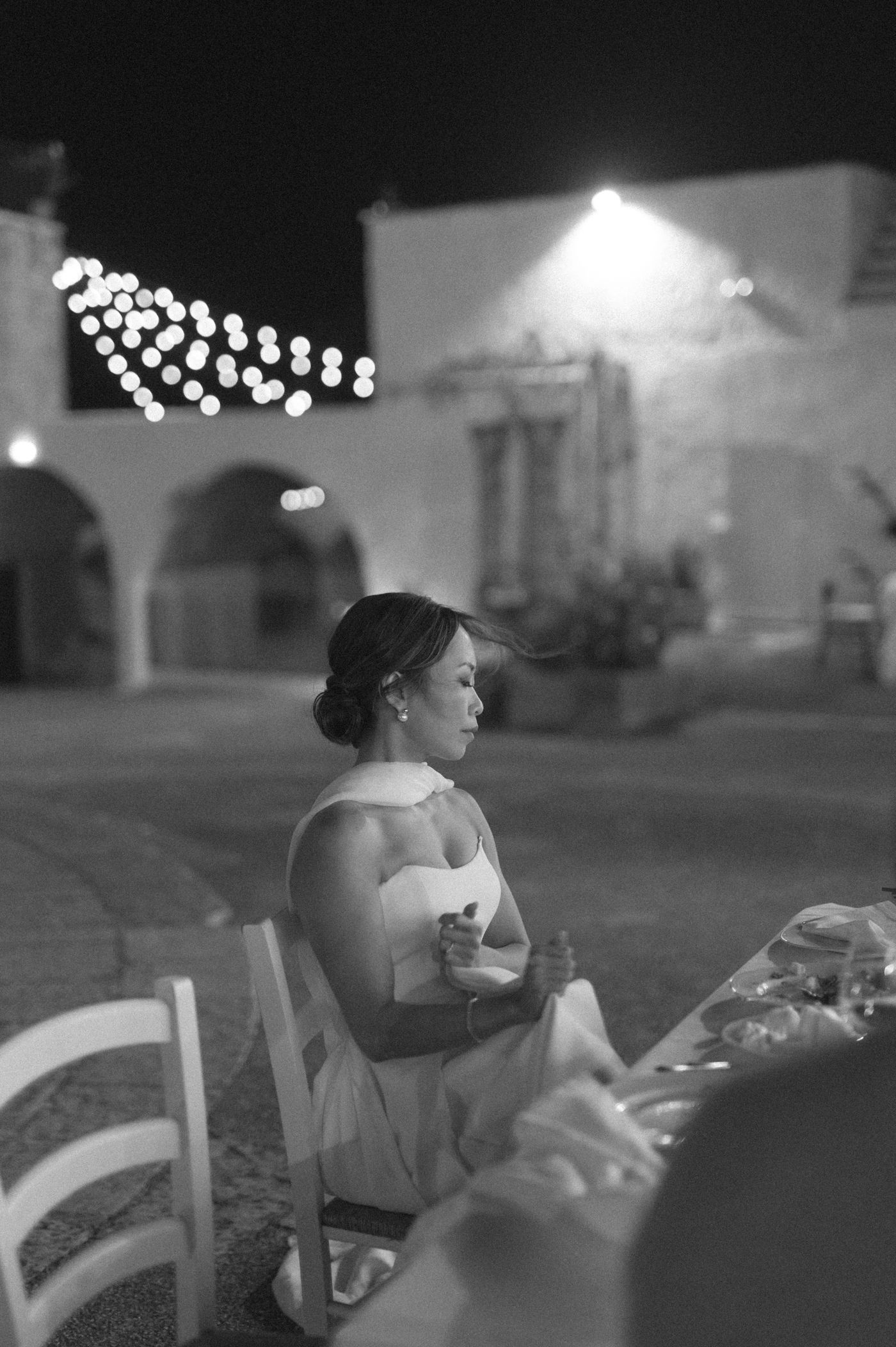 A black and white sequence of images showing a person in a light-colored dress seated outdoors at night.