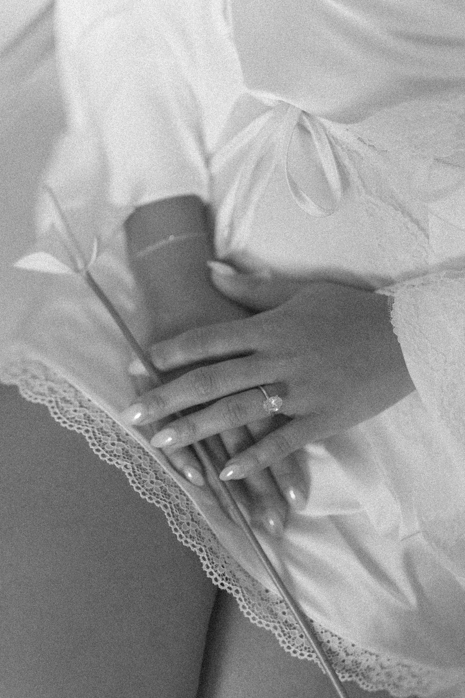 Black and white photo of a bride's hands holding a candle, wearing an engagement ring, in a white lace robe.