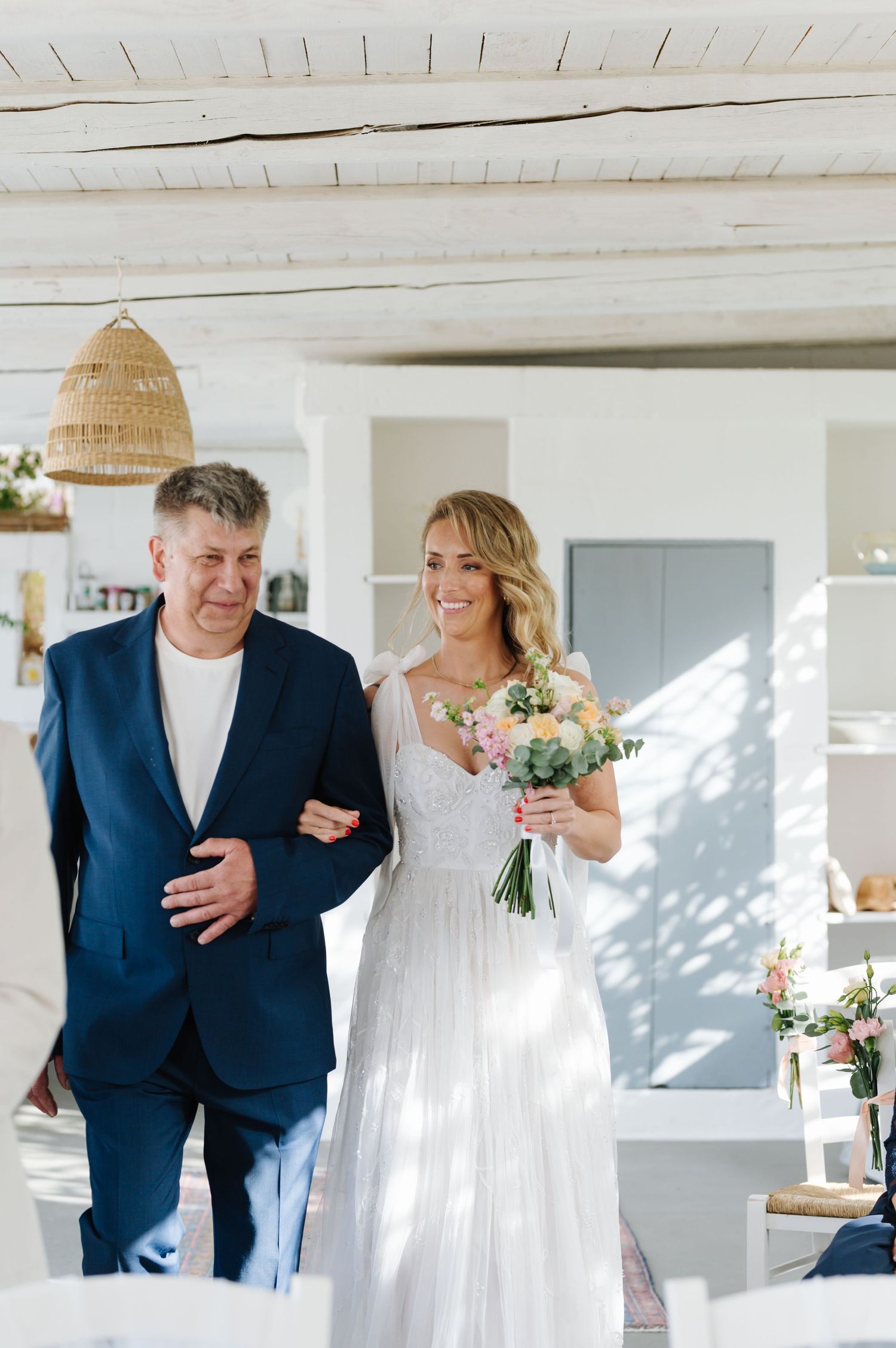 Wedding ceremony in a sunlit white room with wooden ceiling beams.