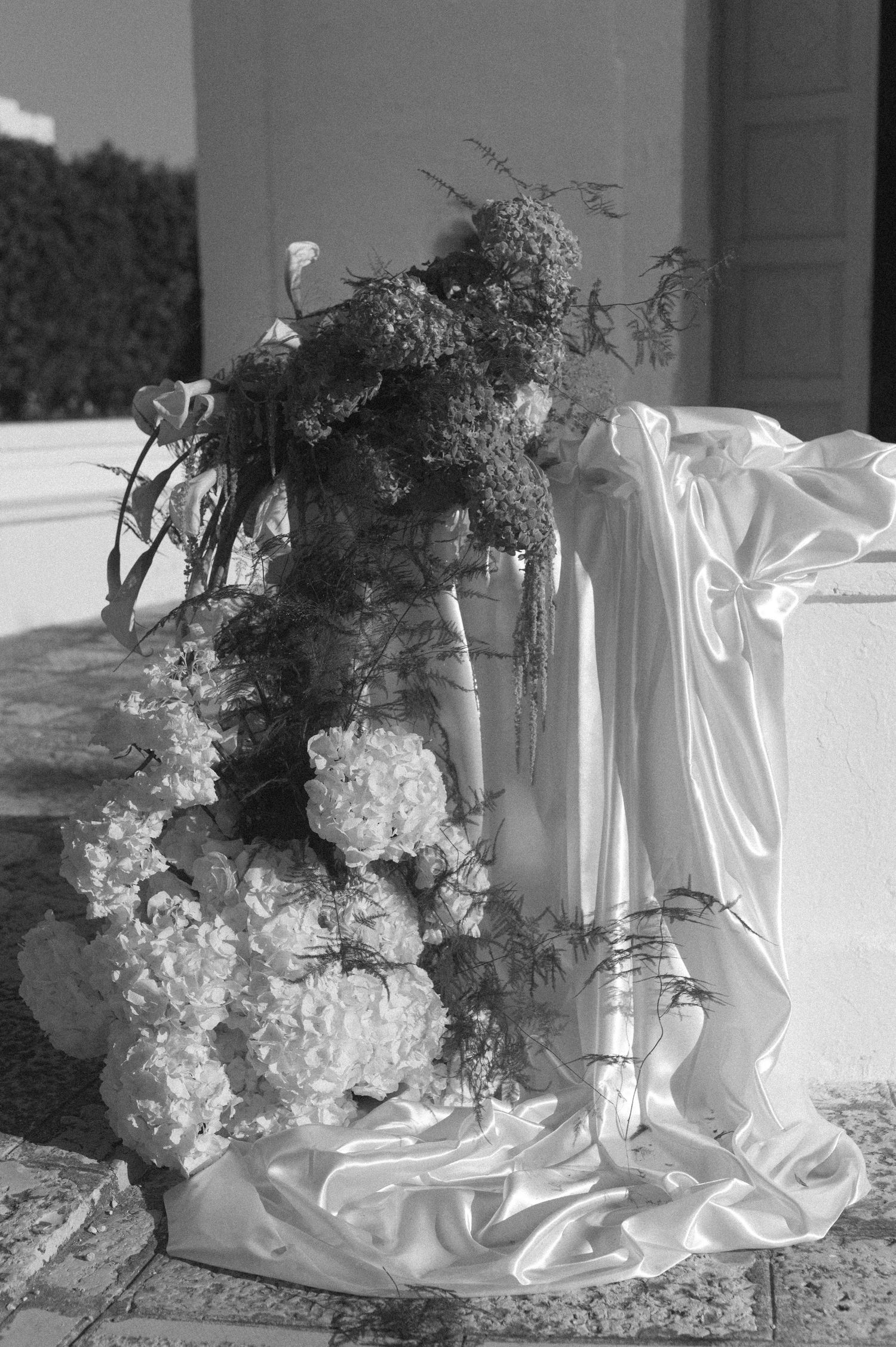 Black and white photo of elegant wedding floral arrangement with hydrangeas and greenery draped in white satin fabric.