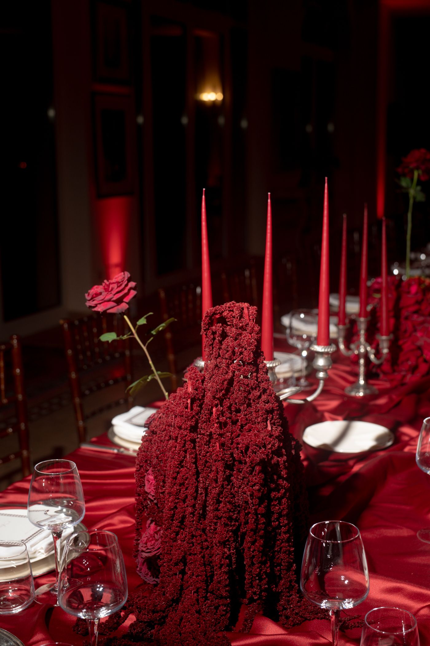Elegant table setting with red tablecloth and tall red amaranthus floral arrangements alongside white taper candles.