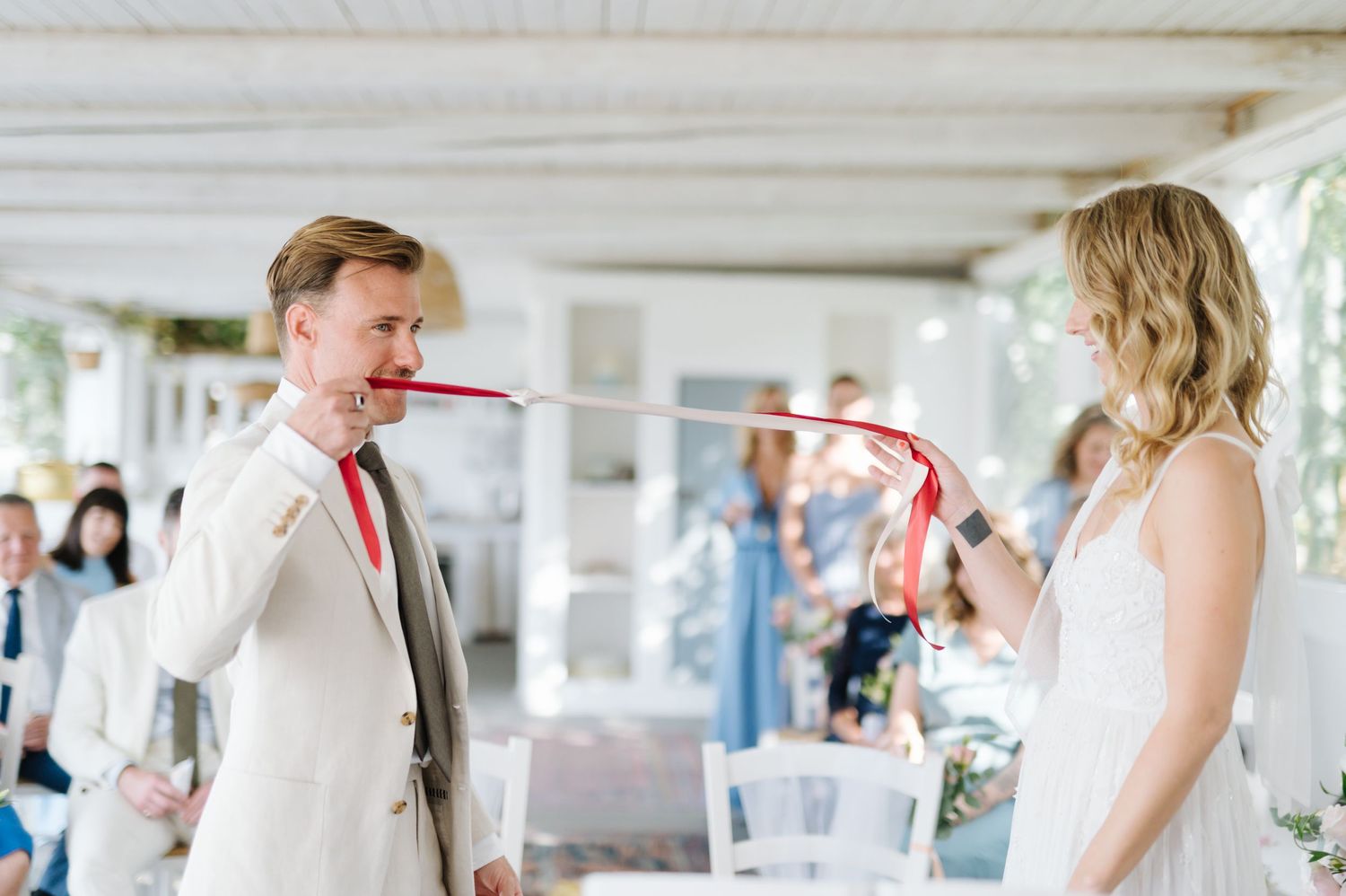 Wedding ceremony in a bright white room with guests looking on as couple exchanges vows.