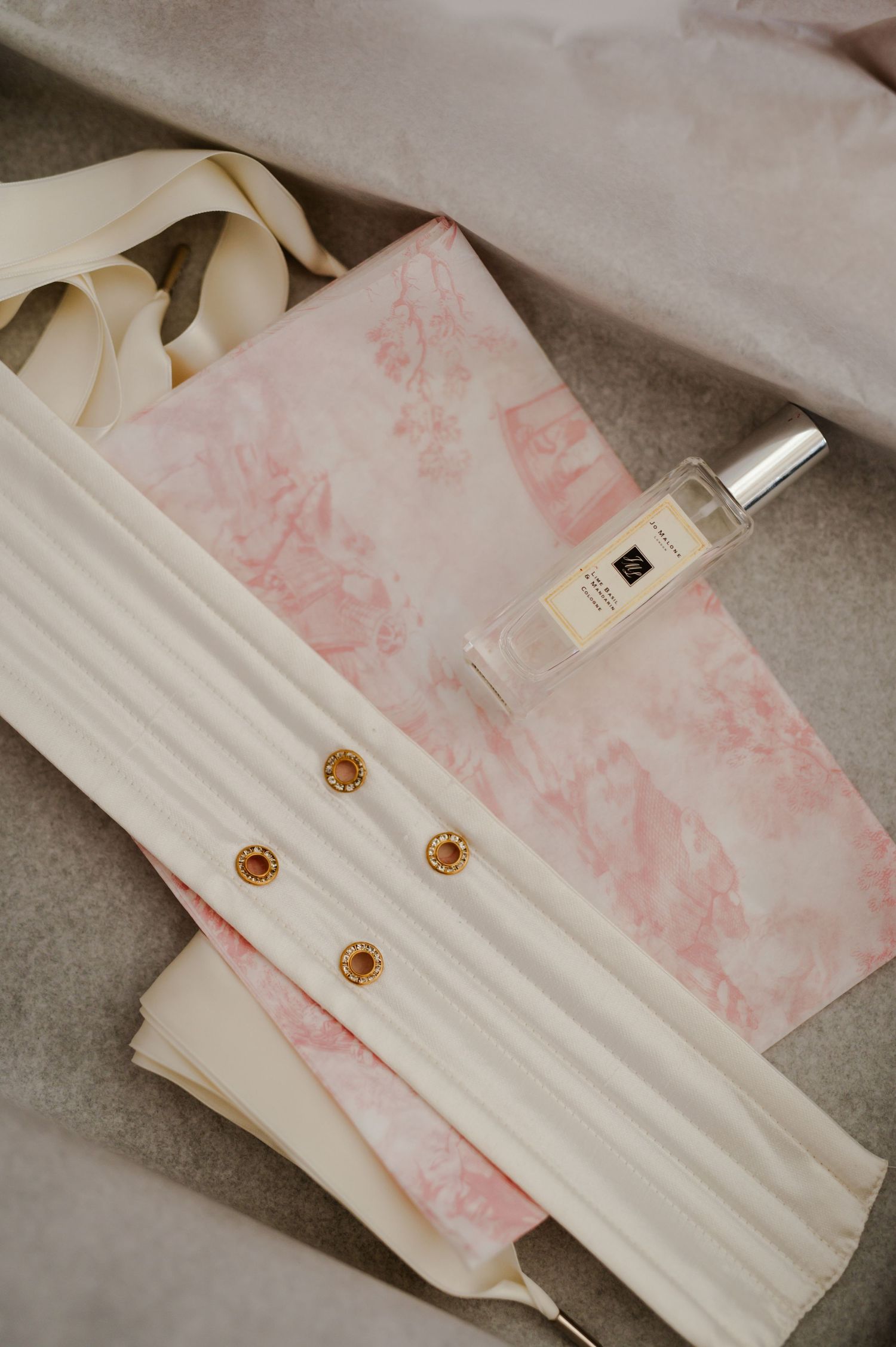 Elegant perfume bottle and white fabric with gold buttons displayed on pink marbled paper.