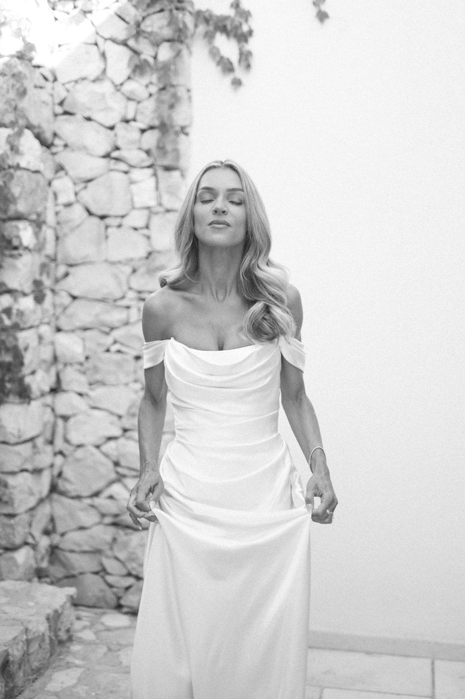 Person in flowing white wedding dress posing against stone wall.