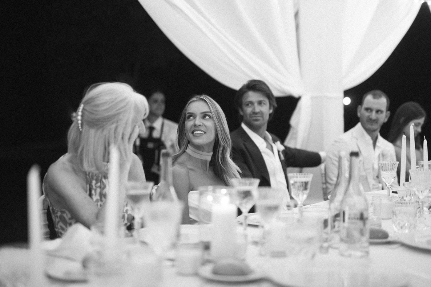 Wedding guests share laughter and conversation at tables decorated with elegant white linens.