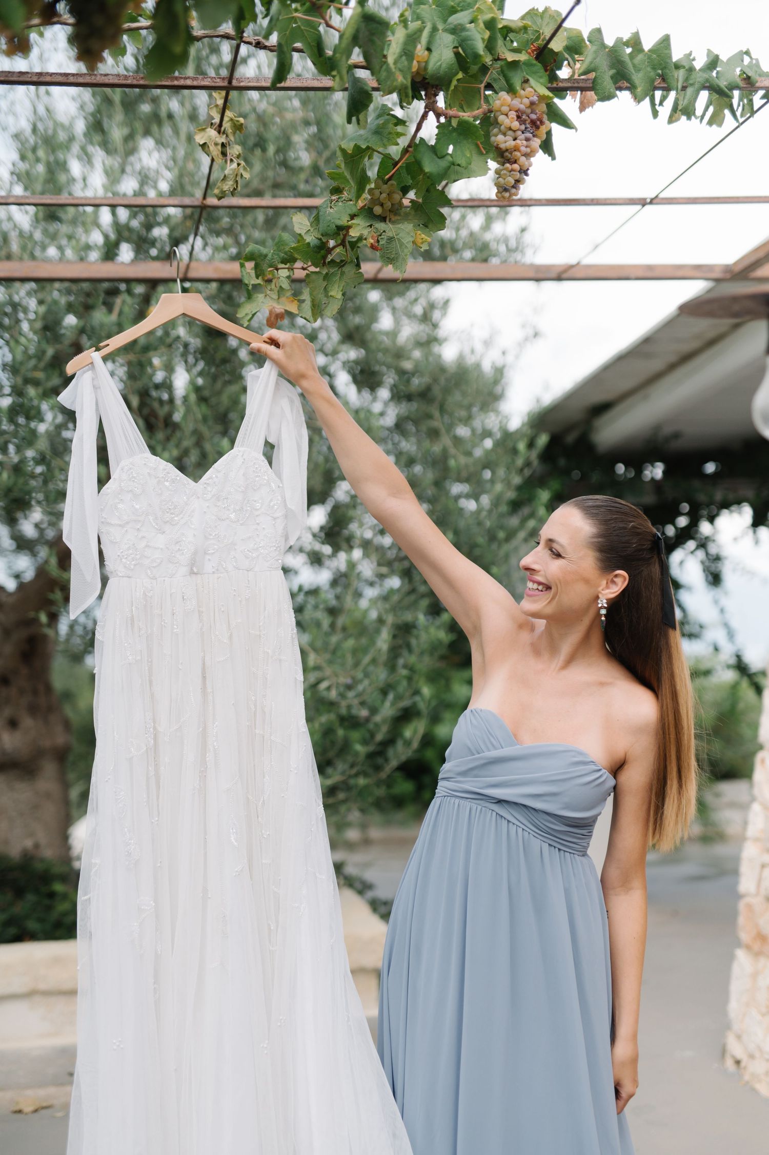 White and dusty blue bridesmaid dresses hanging on outdoor clothesline with greenery backdrop.
