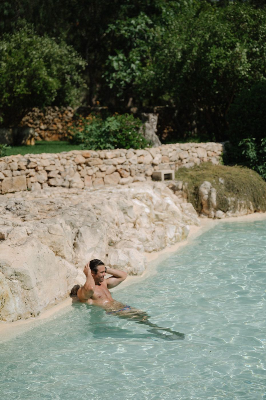 Natural stone pool with crystal clear turquoise water surrounded by greenery.