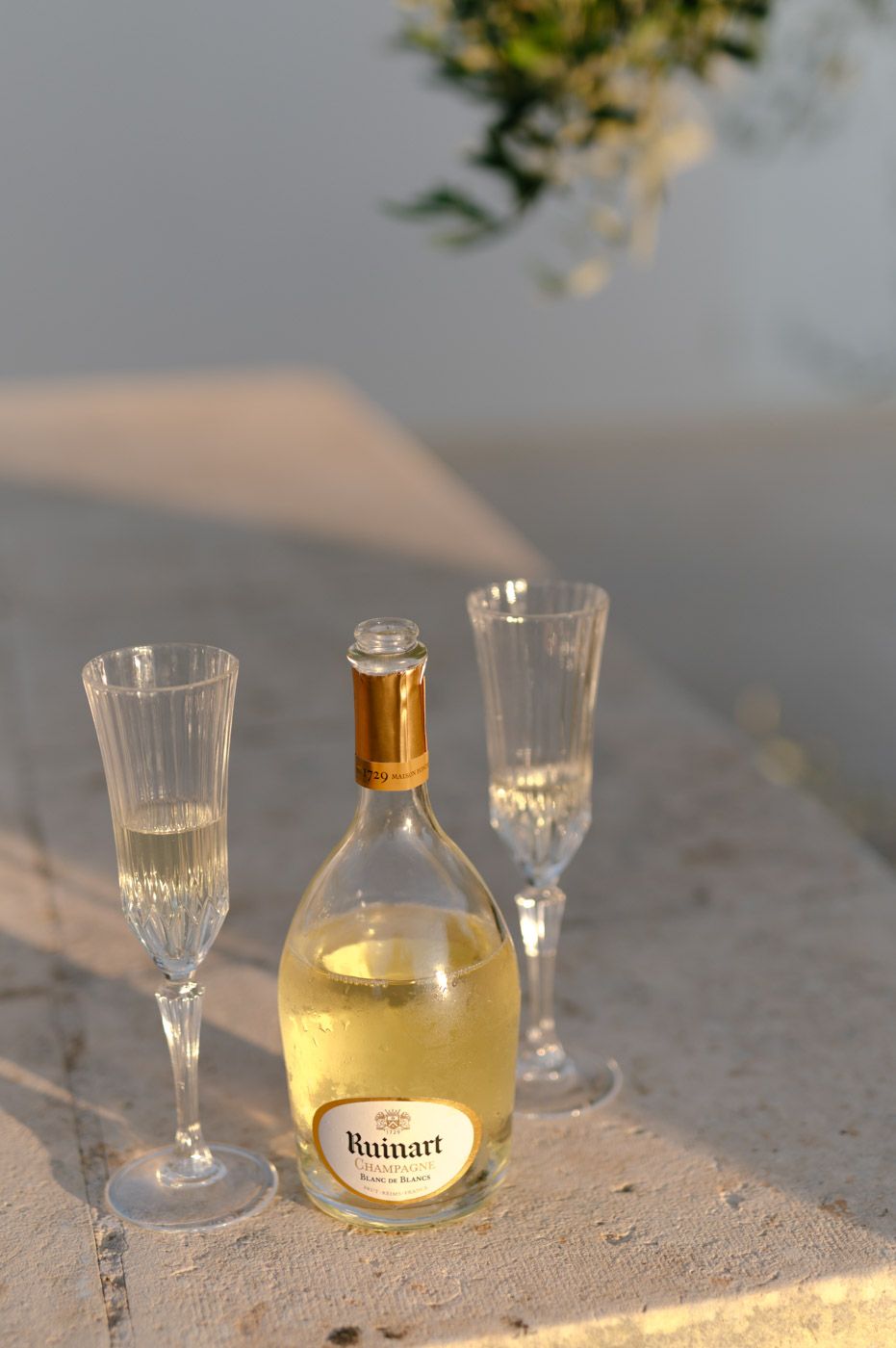 Elegant champagne glasses and a bottle of Ruinart set against a sunset backdrop.