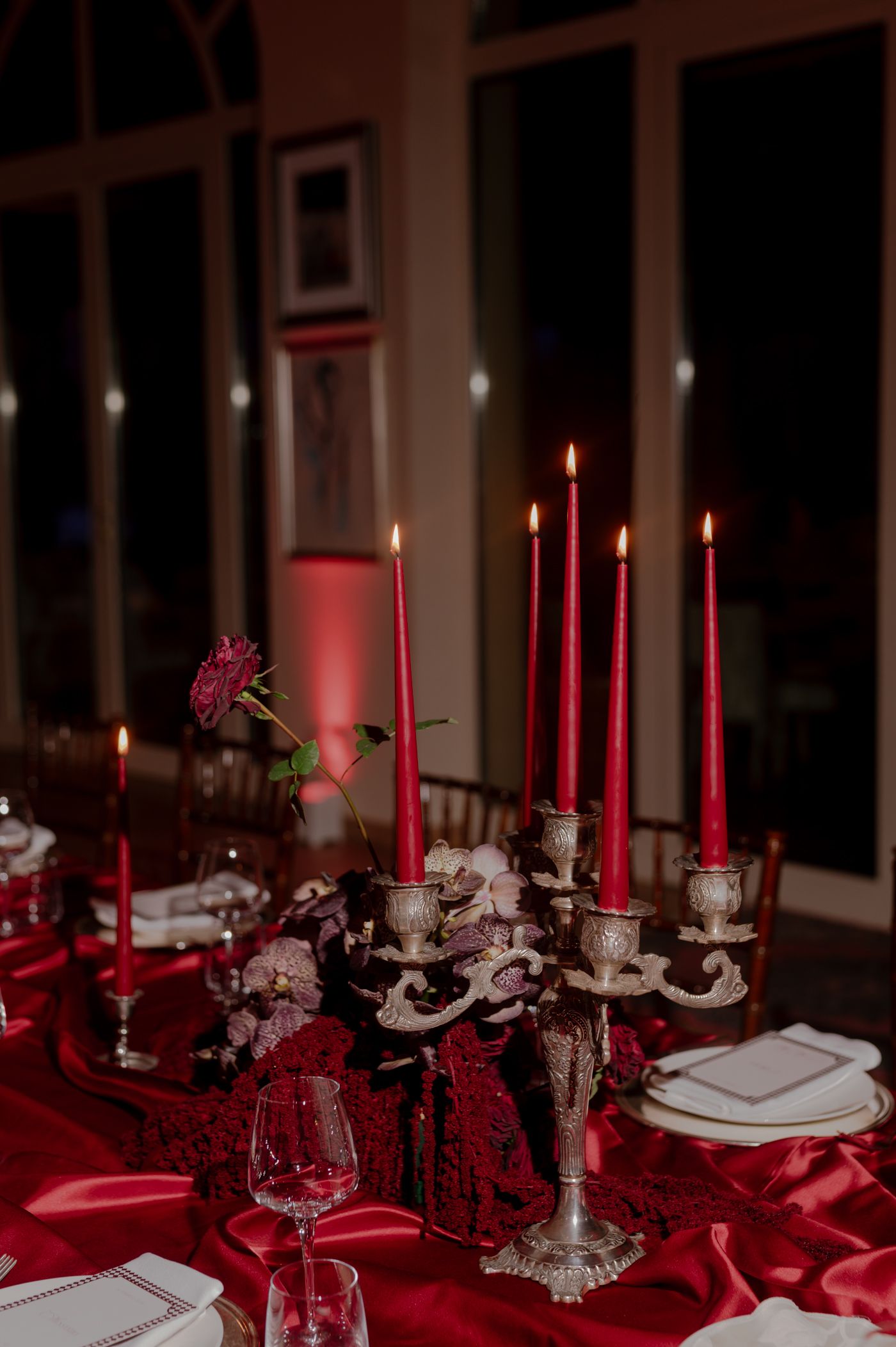 Elegant red table setting with silver candelabra, lit red candles, and wine glasses on a crimson tablecloth.
