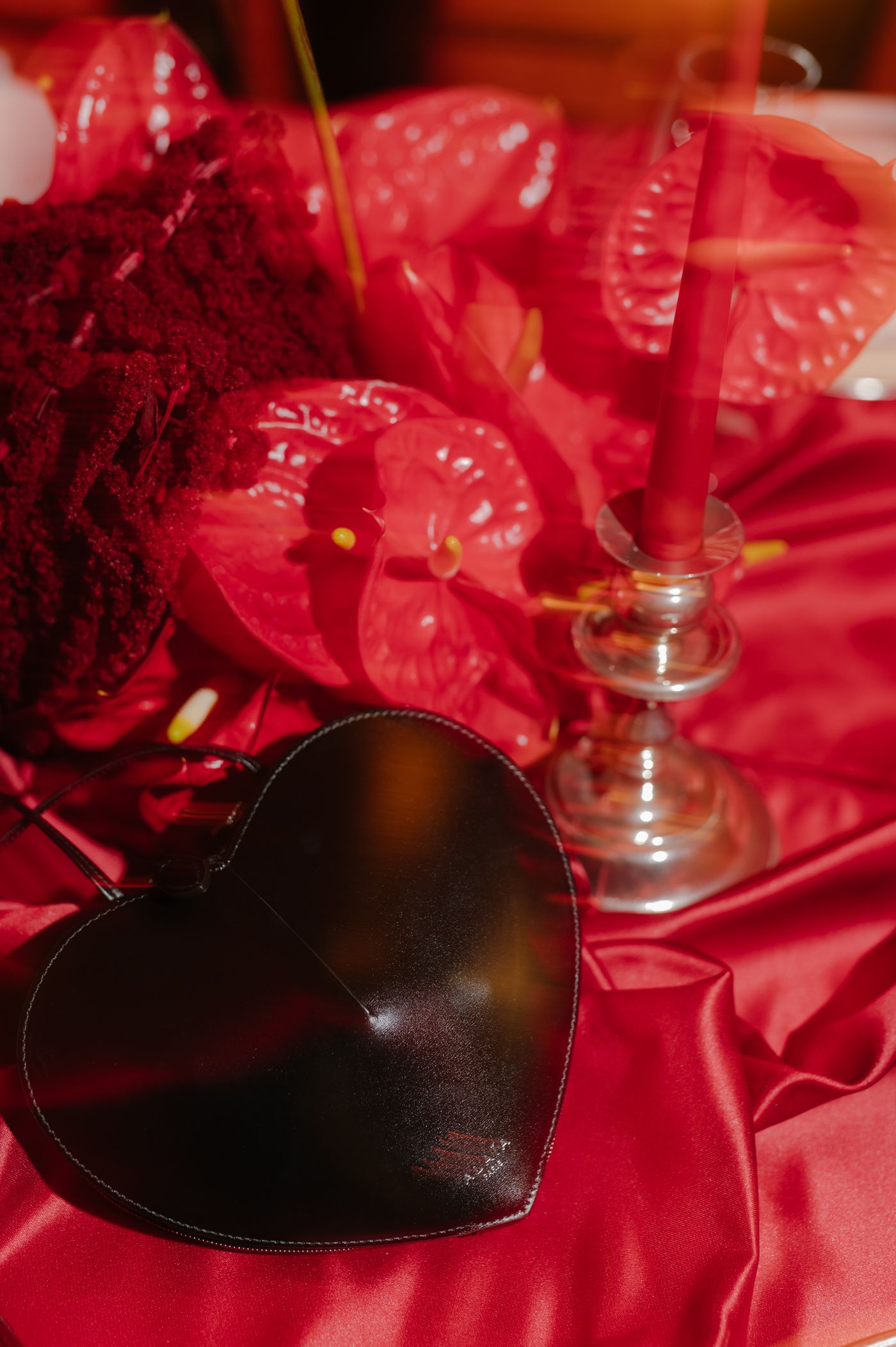 A black heart-shaped decoration rests on red satin fabric next to stemware in a romantic table setting.
