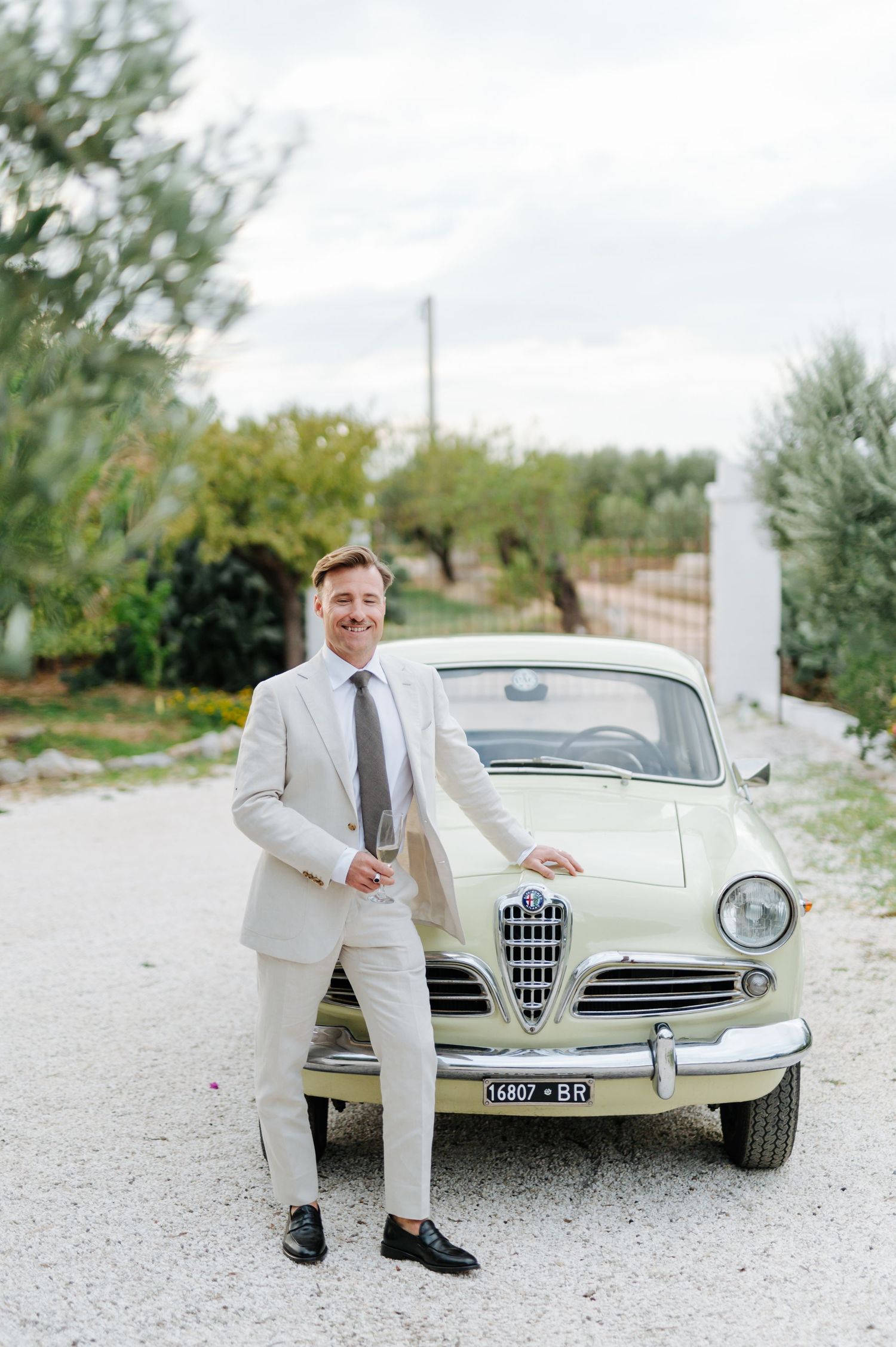 Classic Alfa Romeo vintage car in cream color parked on gravel path.