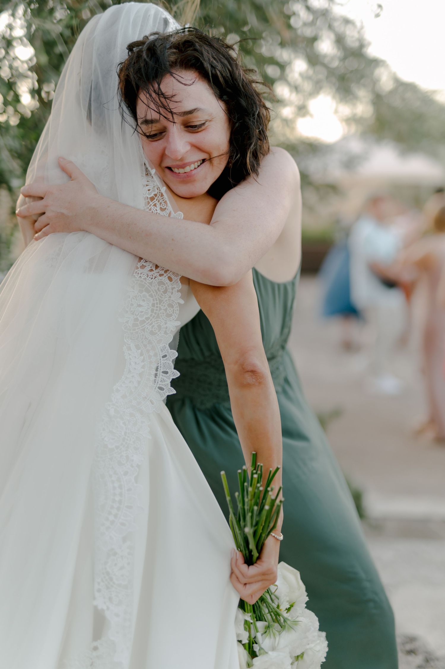 A tender moment between two people in wedding attire embracing during an outdoor ceremony.