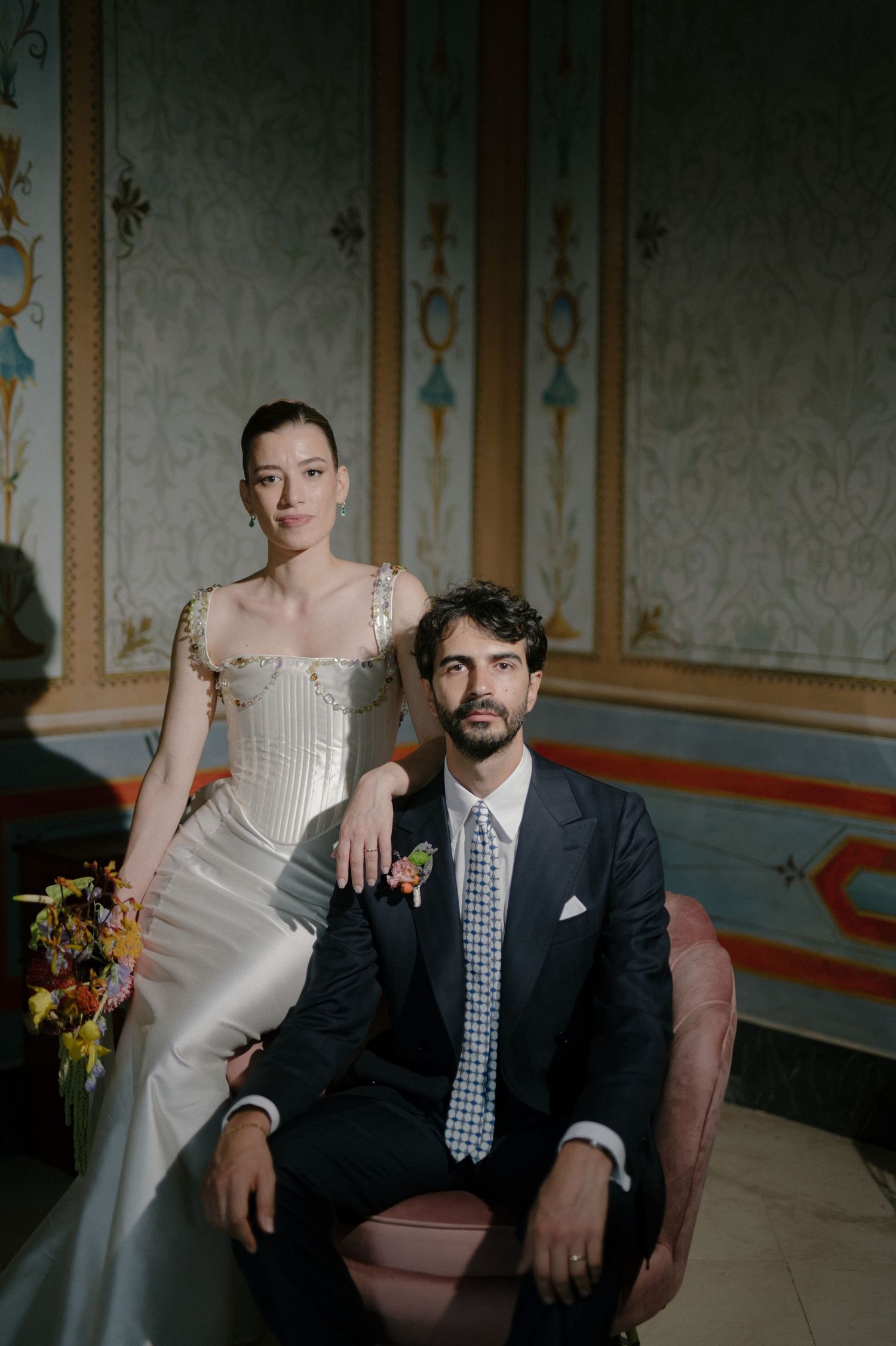 Wedding couple poses elegantly in a vintage room with ornate wall details and moody lighting.