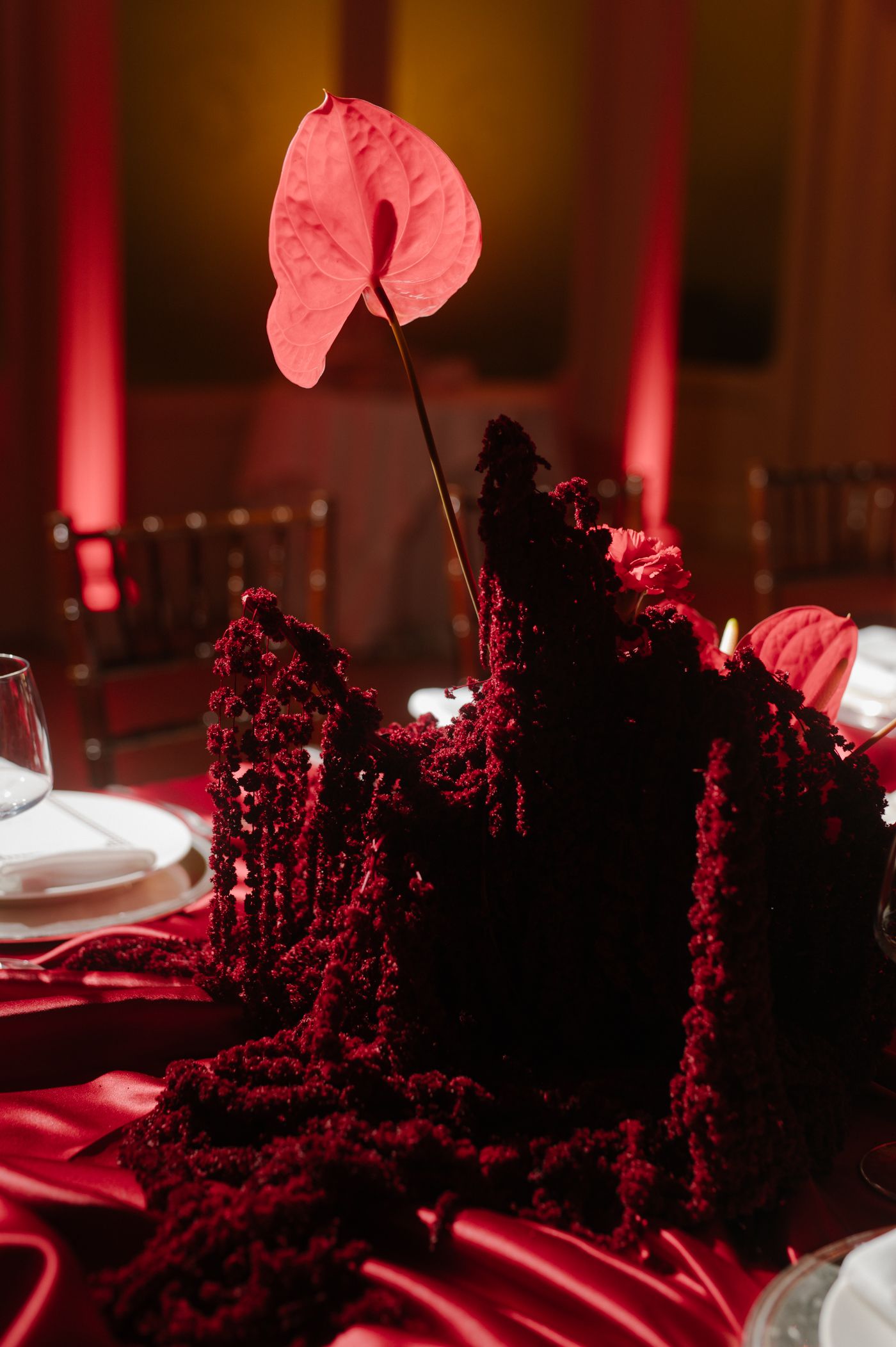 A dark table setting illuminated by red lighting with dramatic shadows and textured centerpieces.
