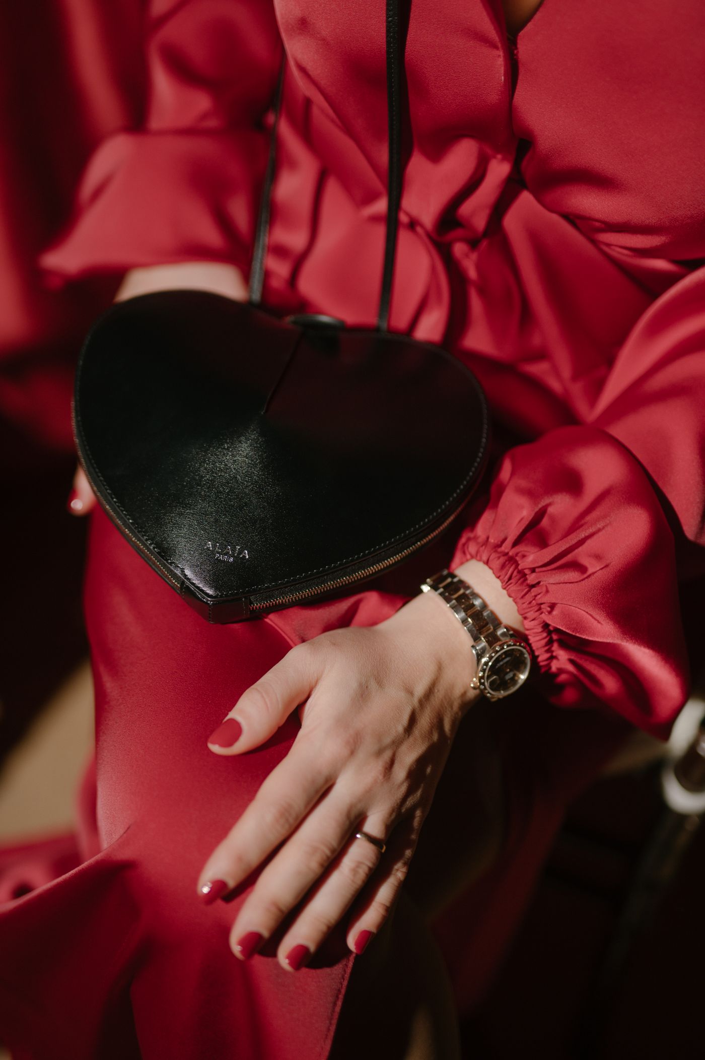 A hand wearing a gold ring rests elegantly against a luxurious red satin fabric background.