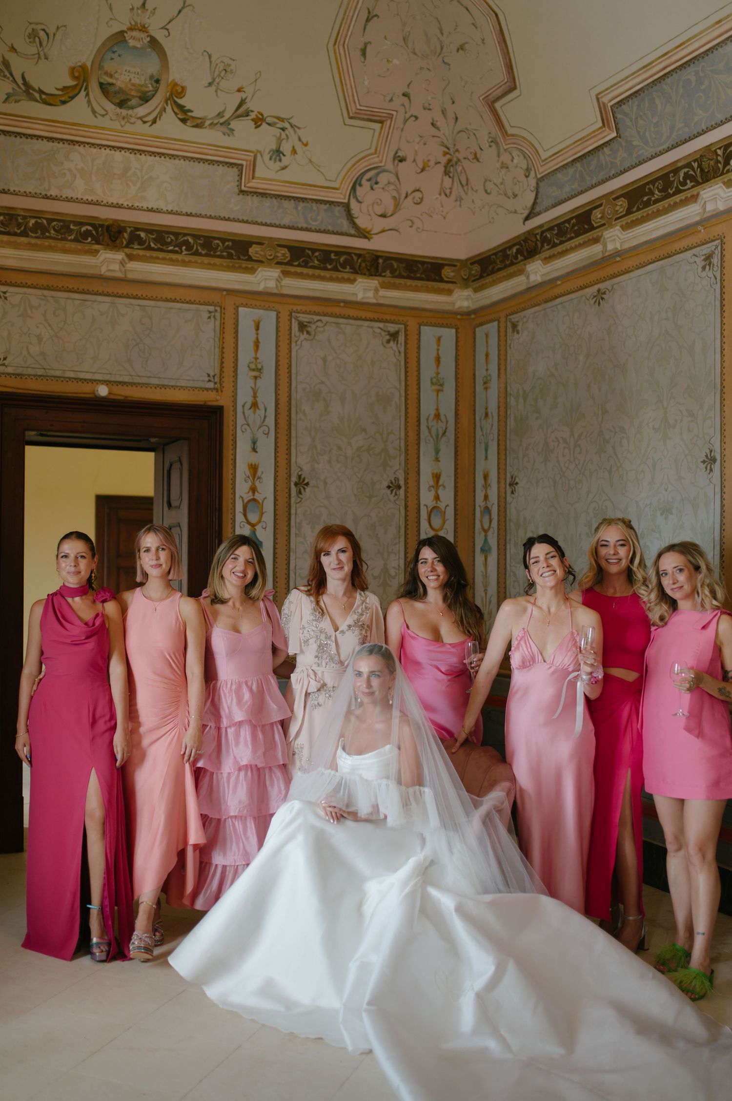 Wedding party group photo in shades of pink and white in an ornate baroque room.