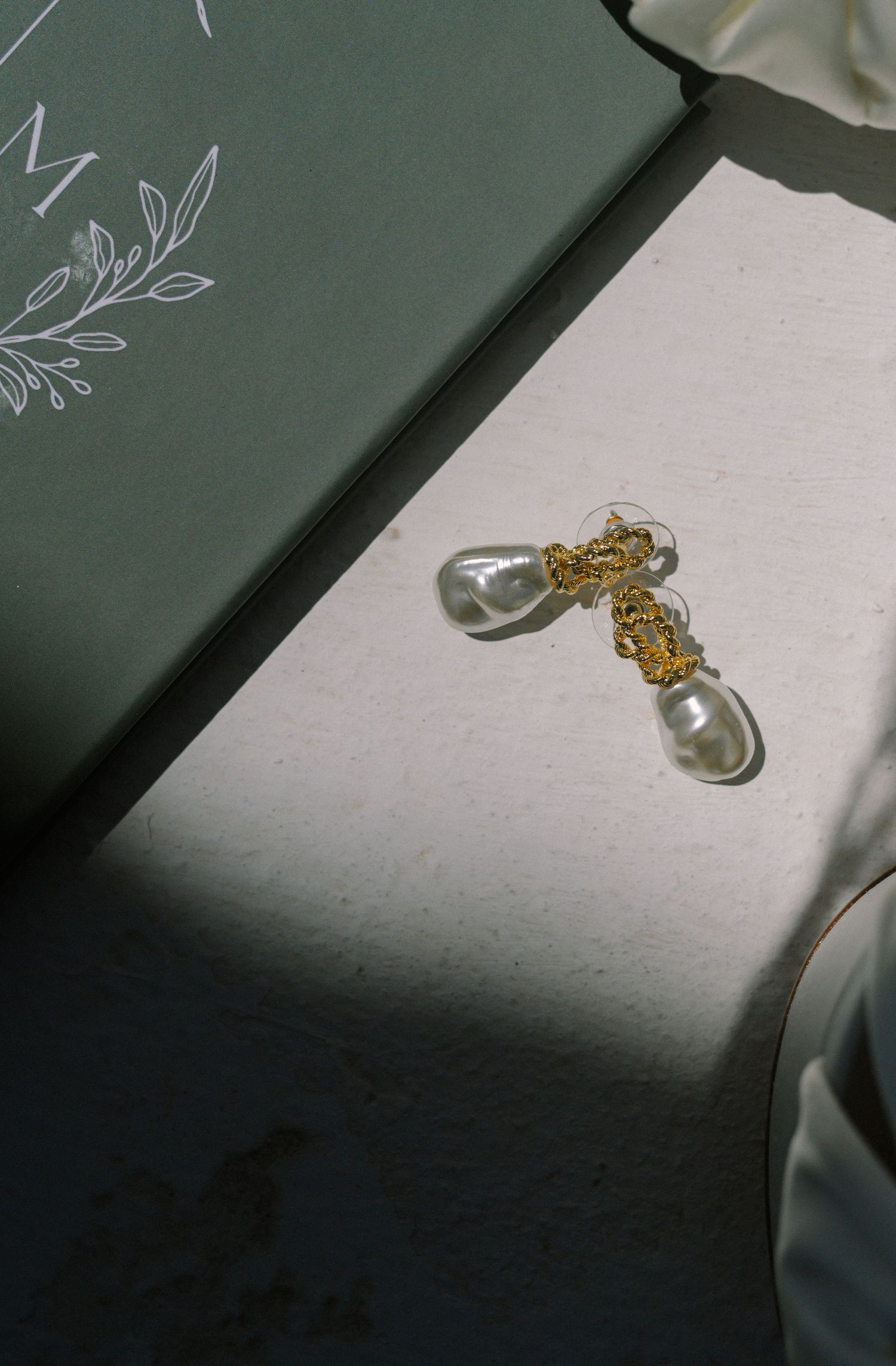 Gold filigree and pearl drop earrings displayed on a white surface beside a sage green gift box.
