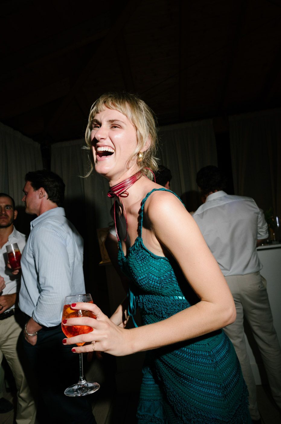 Person in a teal dress enjoying drinks and dancing at a nighttime party celebration.