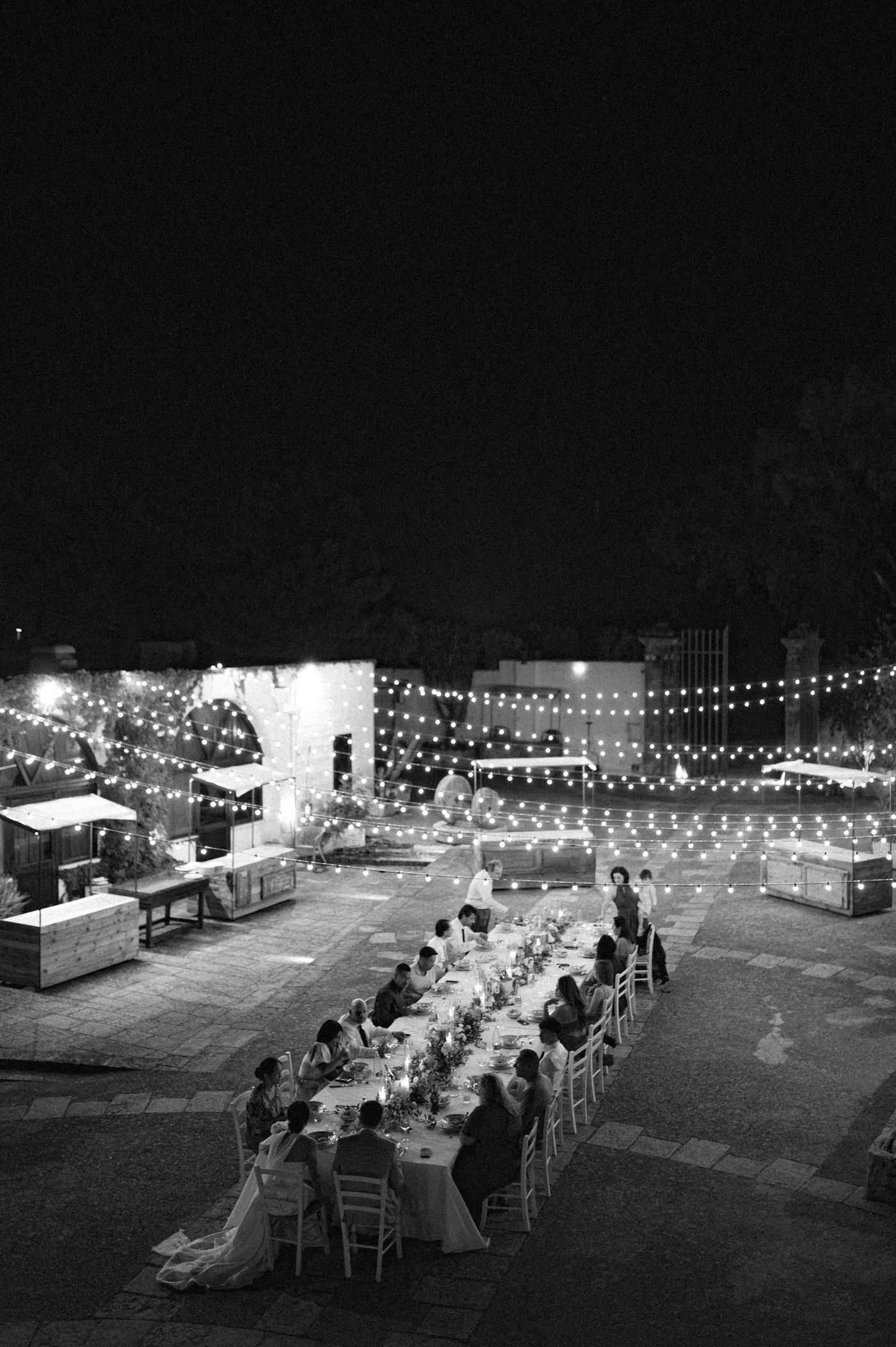 Outdoor evening wedding reception with long tables and string lights creating an elegant ambiance under the night sky.