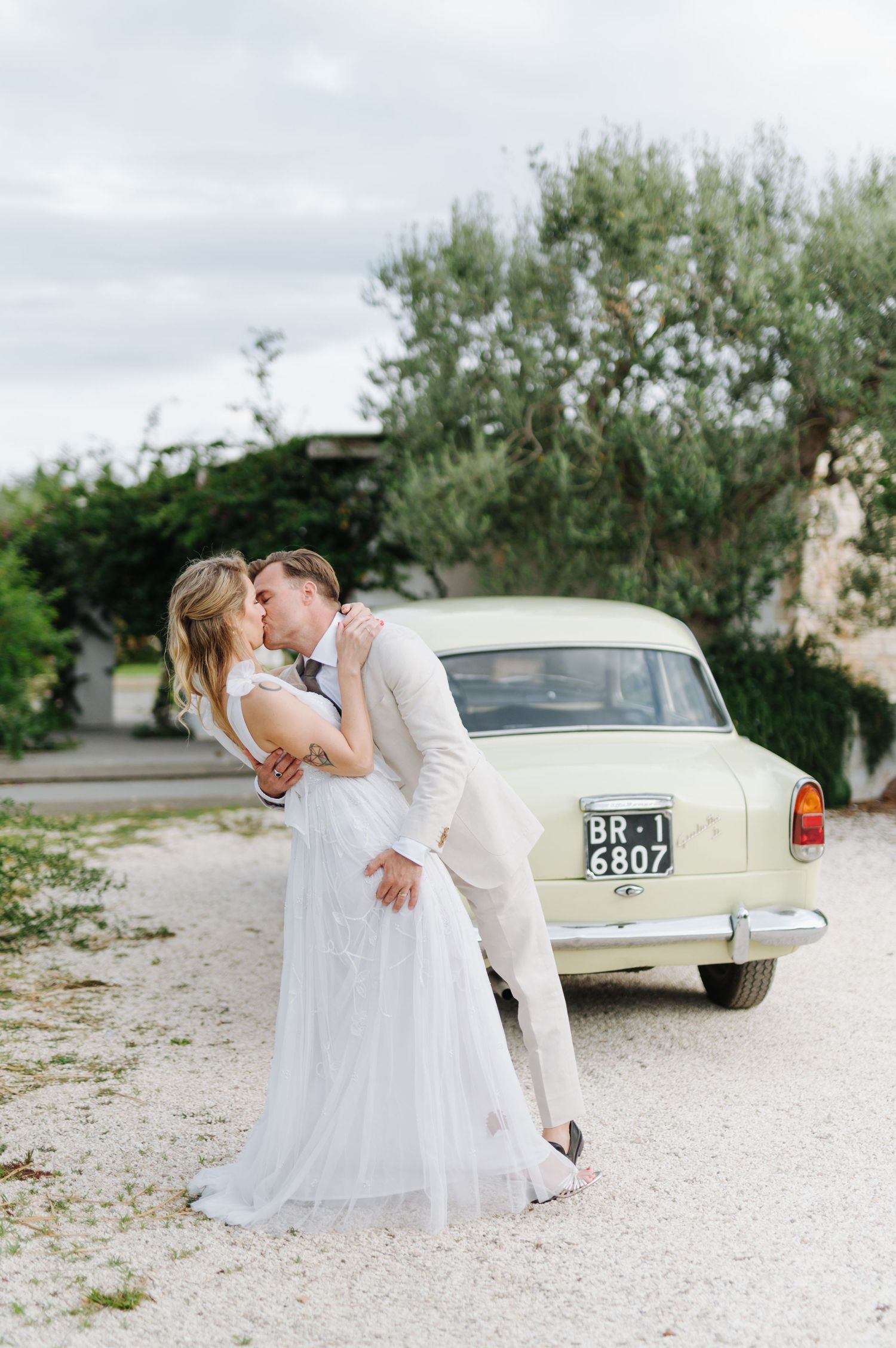 Wedding couple sharing romantic moment near vintage car and Mediterranean architecture.